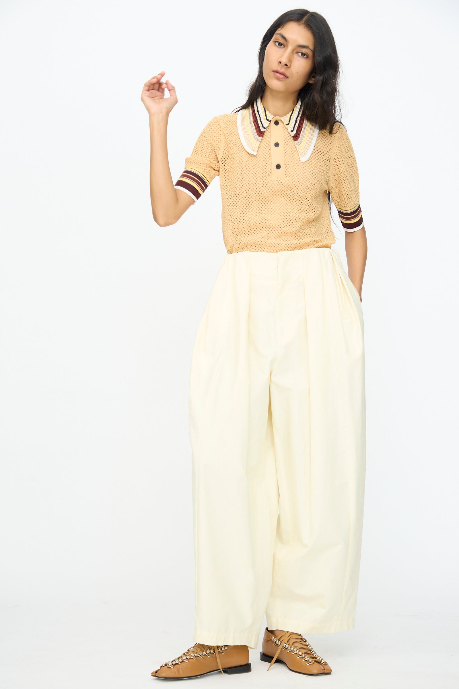 A person stands against a plain background wearing TOGA ARCHIVES' Cotton Ox Wide Pant in Off White, styled with an off-white short-sleeve knit polo and brown shoes for an effortless, oversized look.