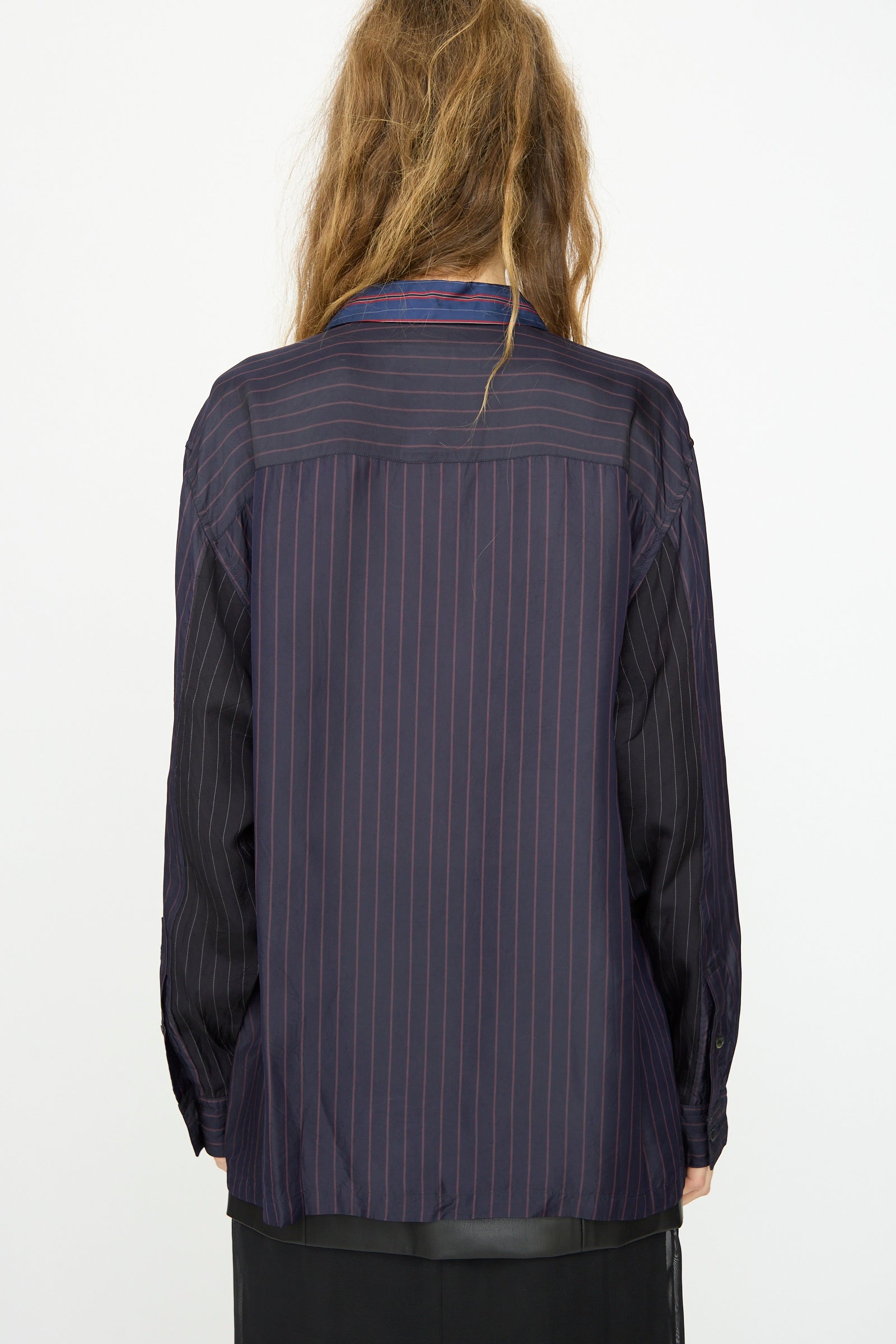 A person with long, wavy hair is seen from behind wearing the TOGA ARCHIVES Cupra Stripe Shirt in Navy over a black skirt against a plain background.