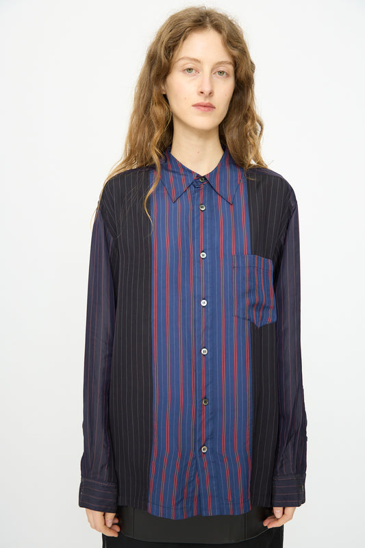 A person with long wavy hair wears the TOGA ARCHIVES Cupra Stripe Shirt in Navy—featuring loose fit, blue and black panels, and red pinstripes—standing against a plain white background.