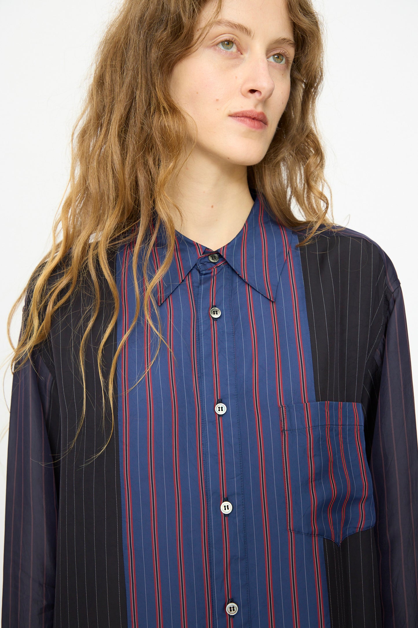 Person with long wavy hair wearing the TOGA ARCHIVES Cupra Stripe Shirt in Navy, featuring blue, red, and black panels, standing against a plain background.