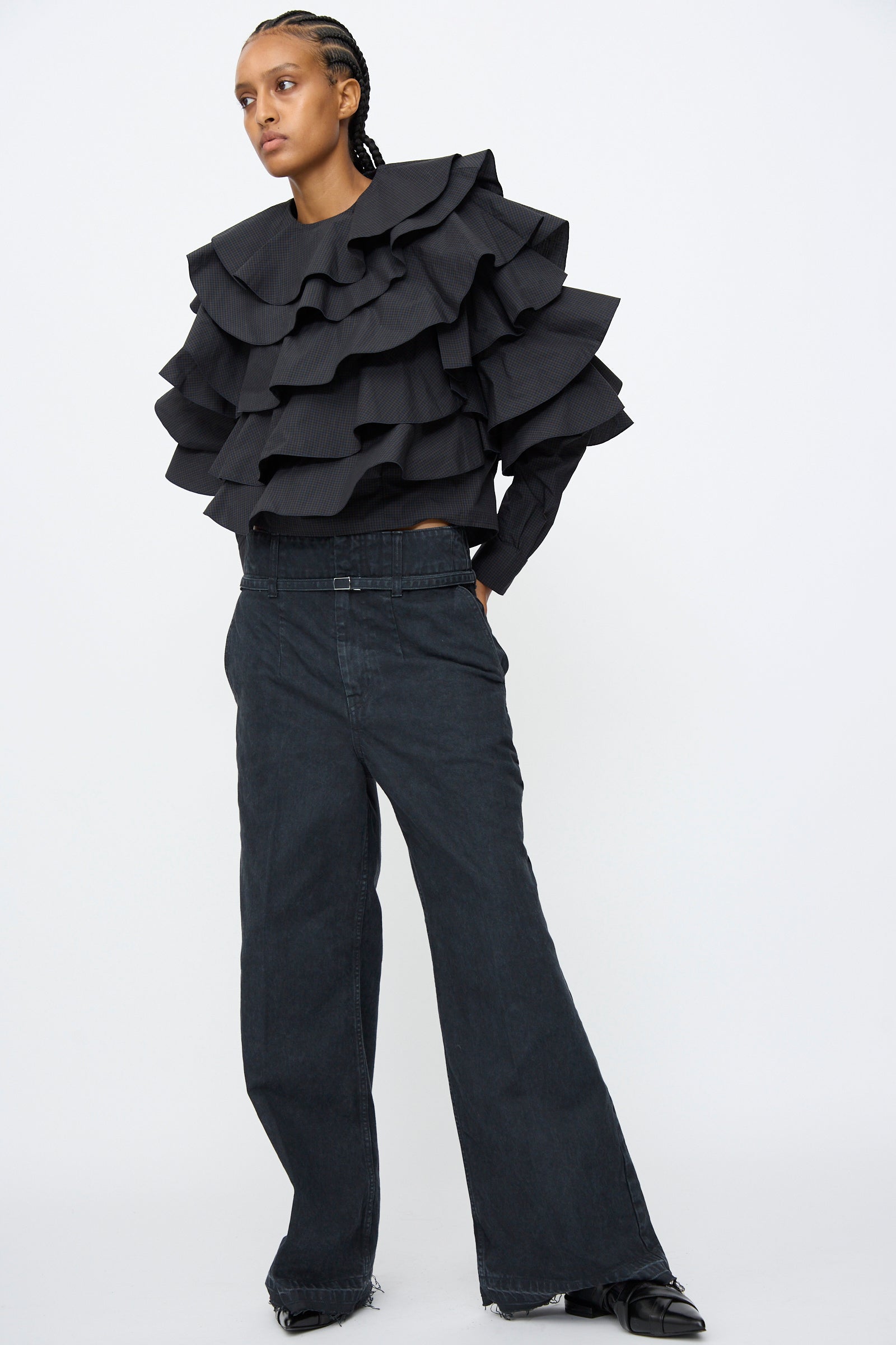 A person wears black Denim Pants by TOGA ARCHIVES, styled with a black ruffled top, standing against a plain white background.