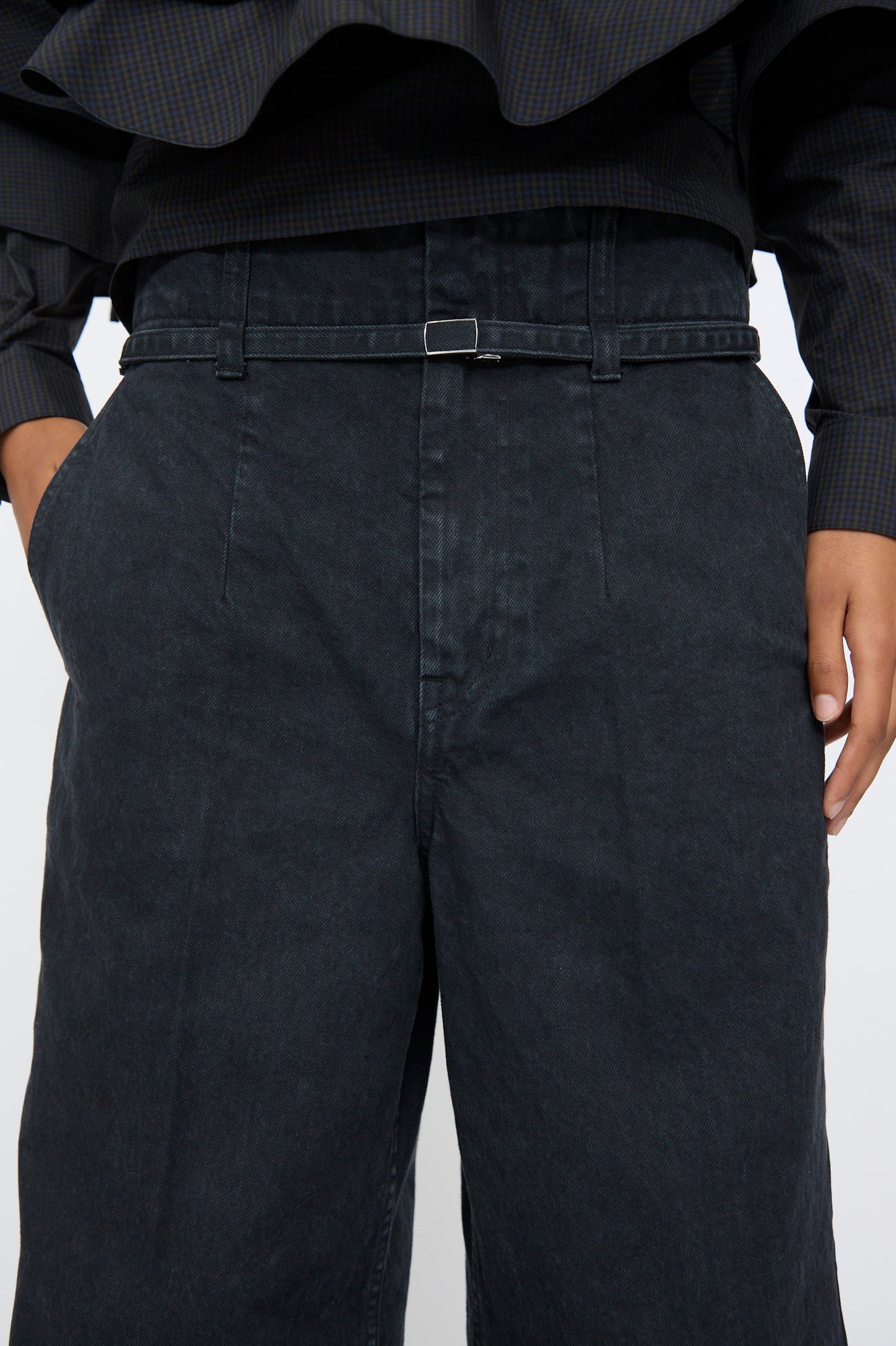A person wearing TOGA ARCHIVES Denim Pants in Black paired with a dark, long-sleeved top and a thin black belt.