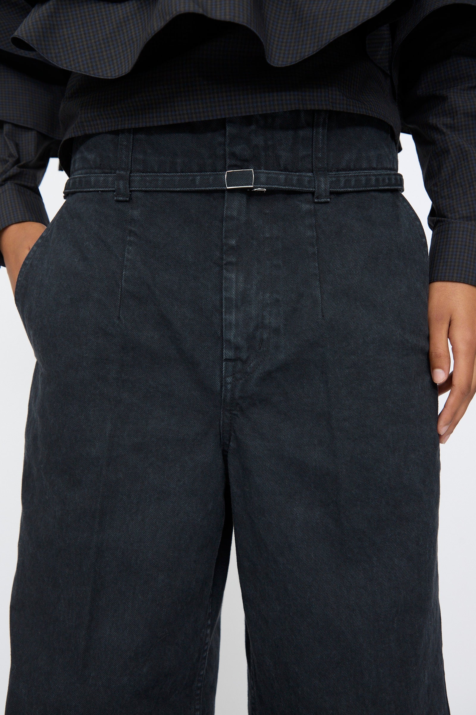A person wearing TOGA ARCHIVES Denim Pants in Black paired with a dark, long-sleeved top and a thin black belt.