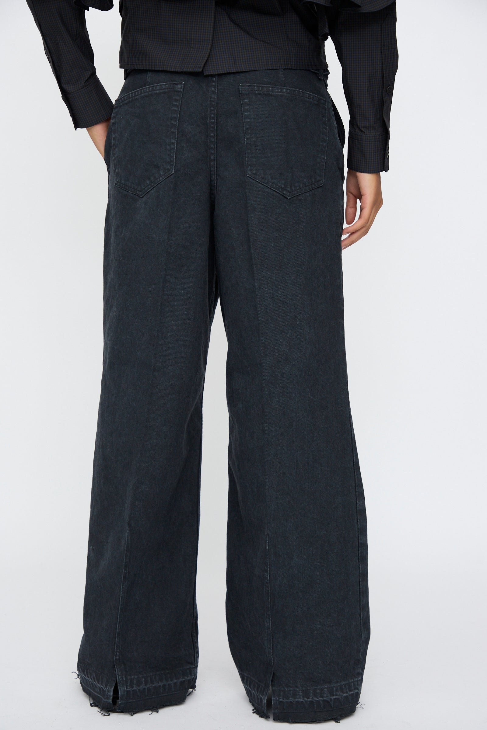 Person wearing TOGA ARCHIVES' Denim Pants in Black, featuring a high-waisted, flared leg design and paired with a black long-sleeve shirt, shown from the back against a plain white background.