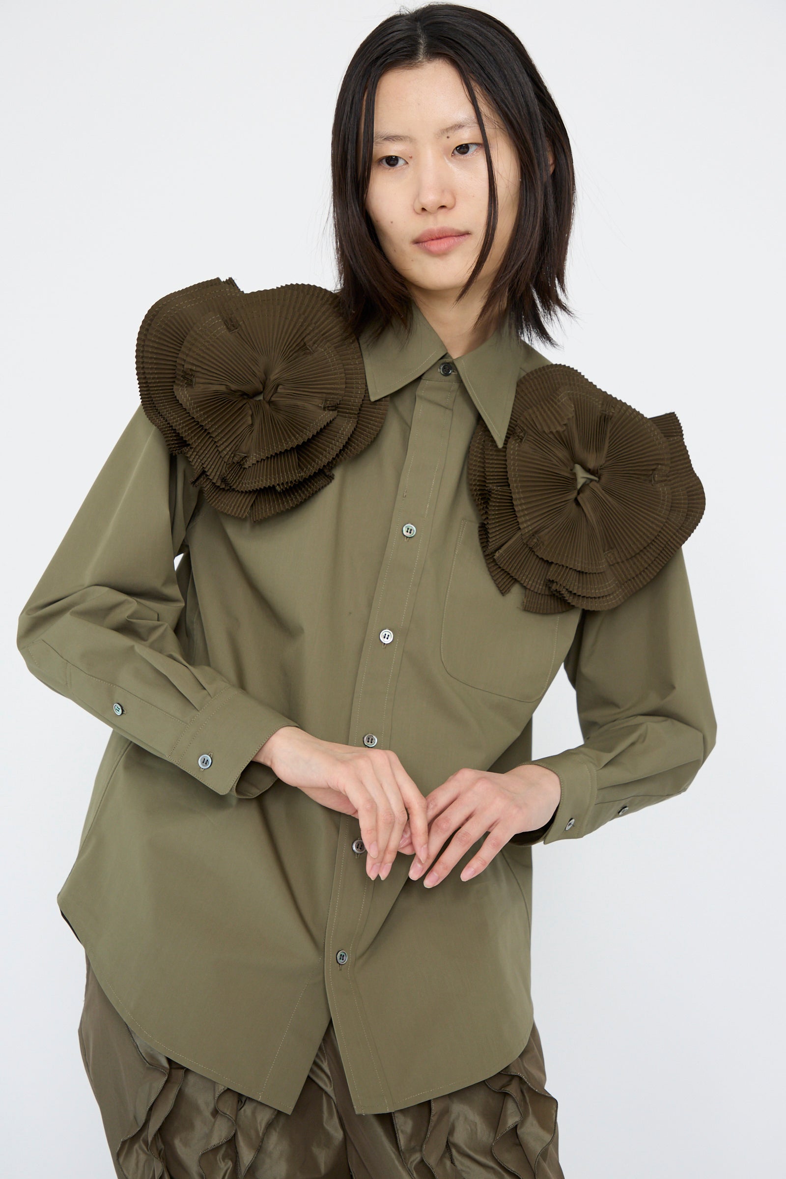 A person in a relaxed fit TOGA ARCHIVES Flower Motif Shirt in Khaki, featuring large ruffled floral shapes on the shoulders, paired with matching pants, stands against a plain background.