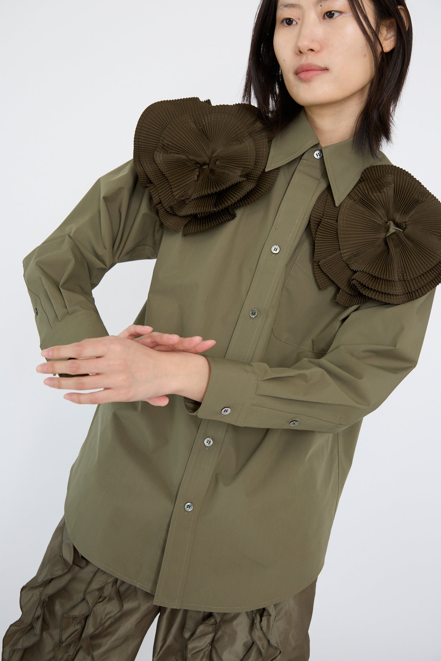 A person wears the TOGA ARCHIVES Flower Motif Shirt in Khaki, a relaxed fit cotton blend shirt with large pleated shoulder accents like ruffled flowers, paired with matching pants against a plain background.