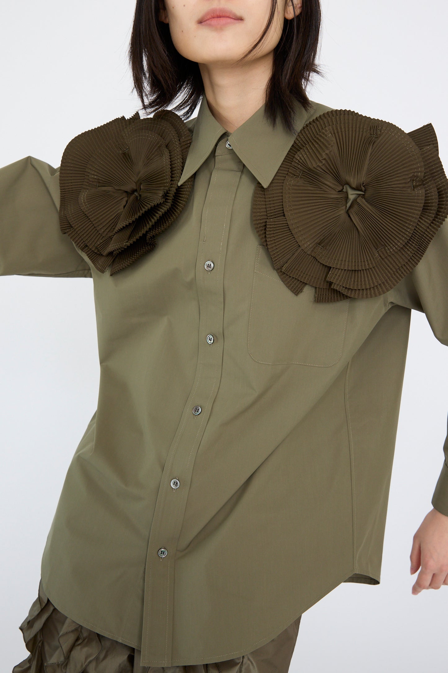 The model is wearing a Flower Motif Shirt in Khaki by TOGA ARCHIVES, featuring a relaxed fit and button-up design with ruffled flower shapes on the shoulders.