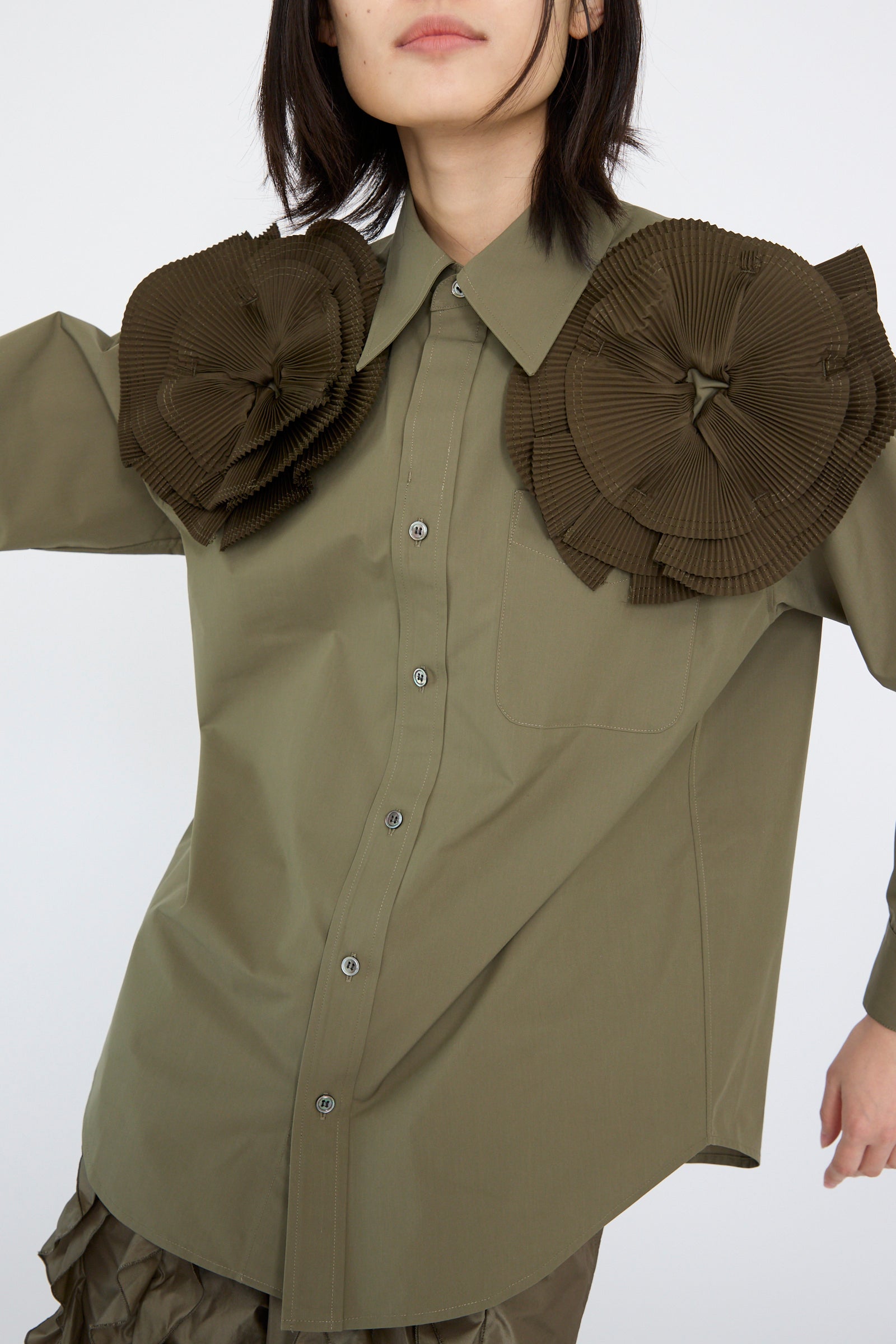 The model is wearing a Flower Motif Shirt in Khaki by TOGA ARCHIVES, featuring a relaxed fit and button-up design with ruffled flower shapes on the shoulders.