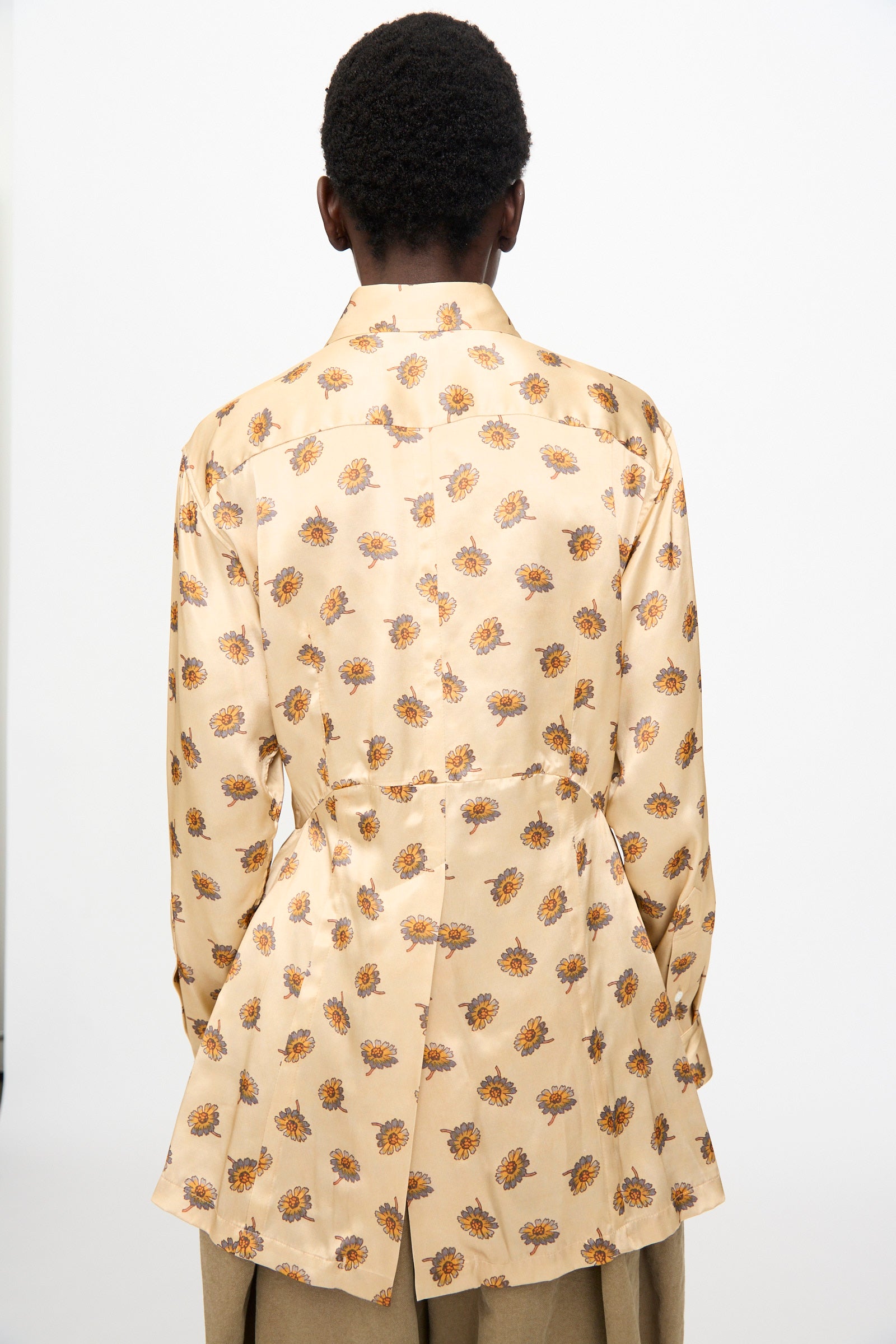 A person faces away from the camera, wearing the TOGA ARCHIVES Flower Print Shirt in Beige, a Japanese-made long sleeve top featuring a floral pattern and tailored back detail.