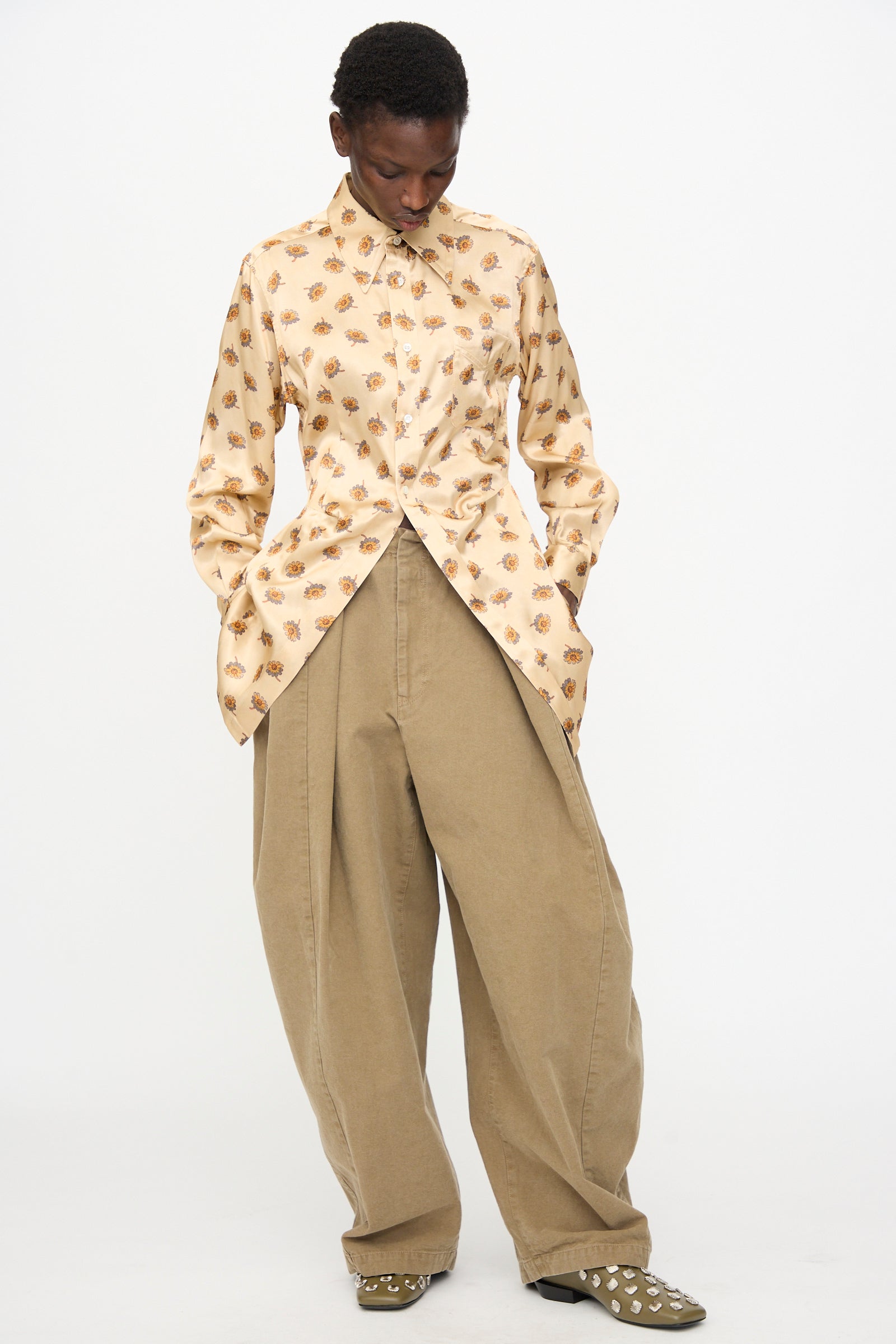 A person wears the TOGA ARCHIVES Flower Print Shirt in Beige and loose khaki pants, standing with hands in pockets against a white background. The shirt is made in Japan, ensuring premium quality and comfort.