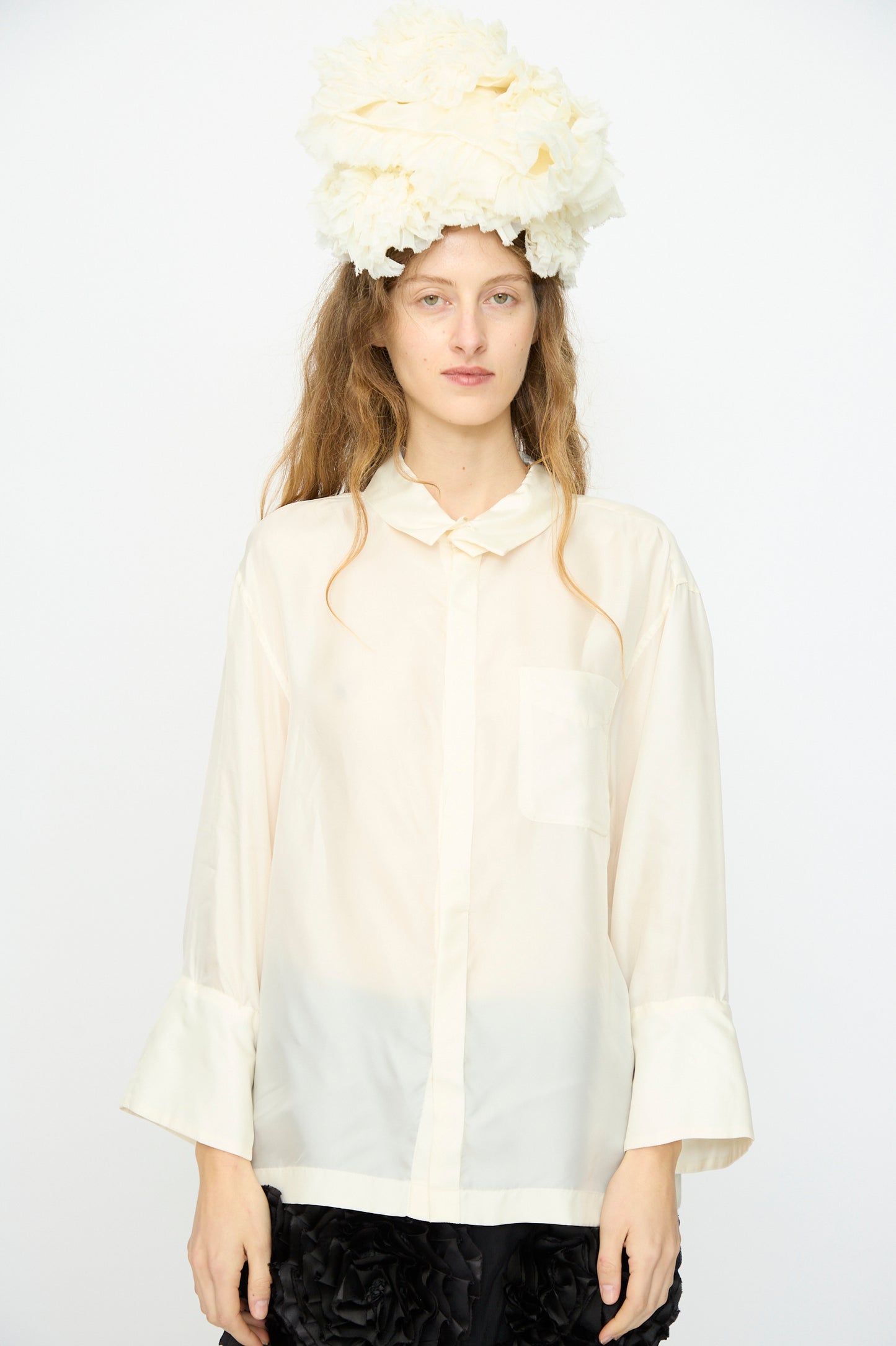 A person wears the TOGA ARCHIVES Frill Embroidery Blouse in Off White and a large textured white headpiece, standing against a plain white background.