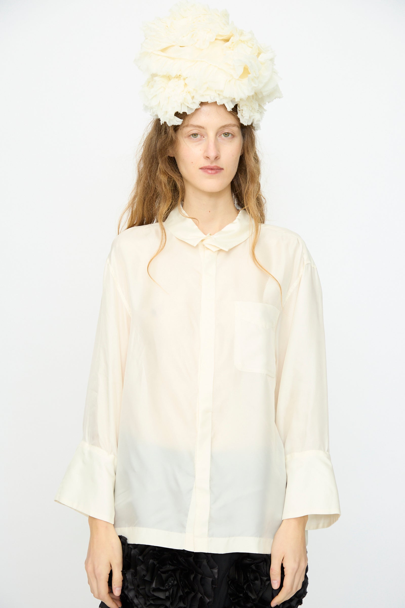 A person wears the TOGA ARCHIVES Frill Embroidery Blouse in Off White and a large textured white headpiece, standing against a plain white background.
