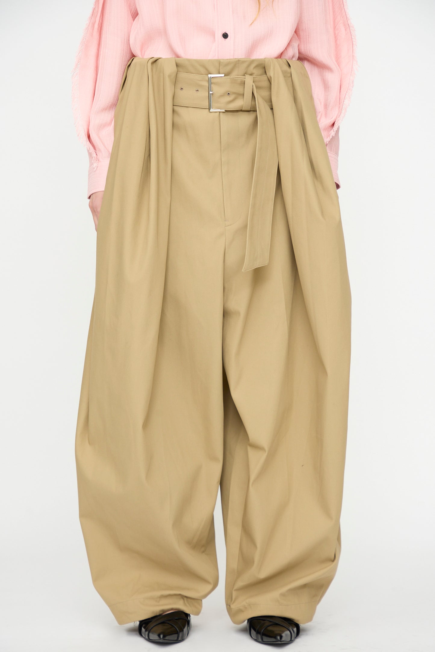 A person wears TOGA ARCHIVES High Twist Twill Wide Pants in Beige with a pink shirt tucked in, standing against a plain white background.