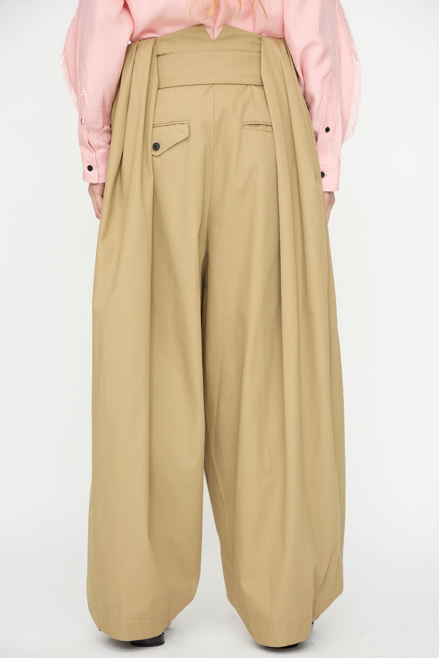A person is seen from the back wearing TOGA ARCHIVES High Twist Twill Wide Pants in Beige with a light pink shirt, photographed against a plain white background.