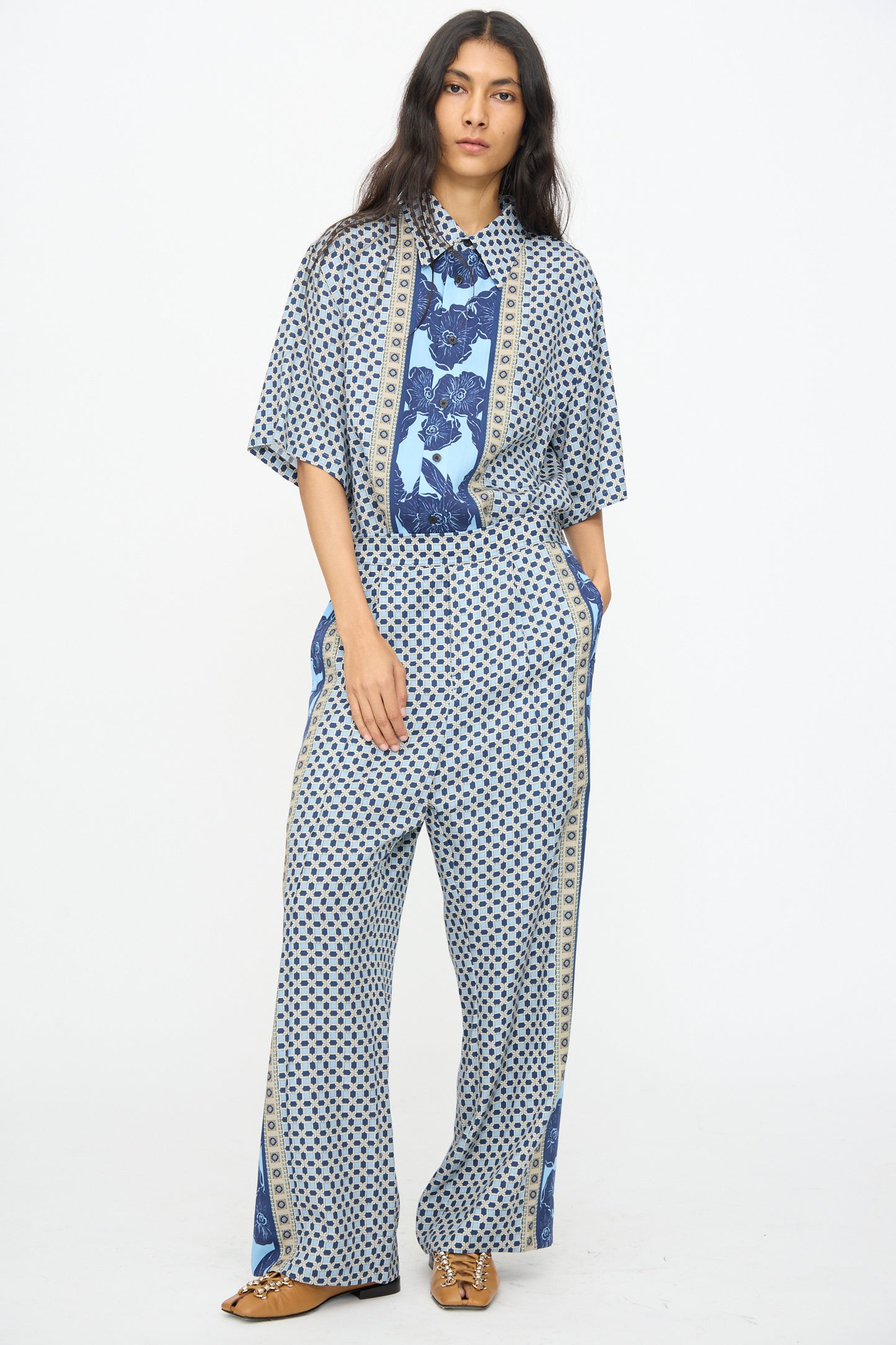 A person stands against a plain background wearing TOGA ARCHIVES’ Inner Print Pant in Light Blue with a loose-fitting geometric shirt and tan shoes—an effortlessly chic Japanese-made look.