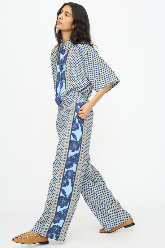 A woman wears the TOGA ARCHIVES Inner Print Pant in Light Blue with a loose top and tan flat shoes, standing against a plain white background.