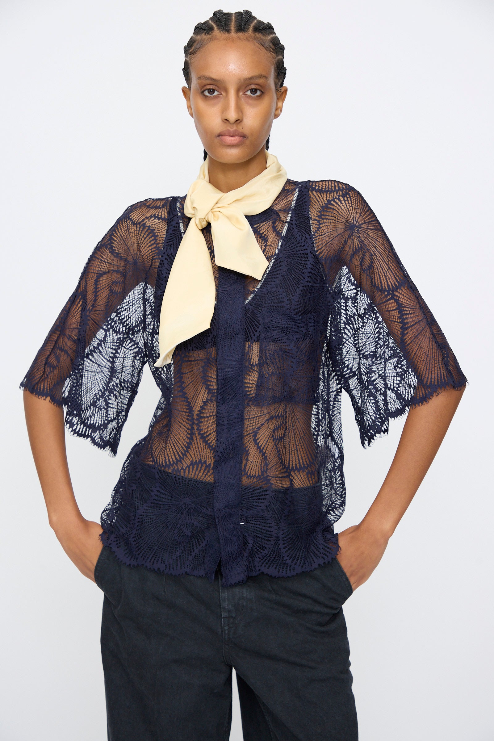 Model wears the TOGA ARCHIVES Lace Blouse in Navy with an oversized fit over a dark top, paired with black pants and a light beige neck scarf, standing hands on hips against a plain background.