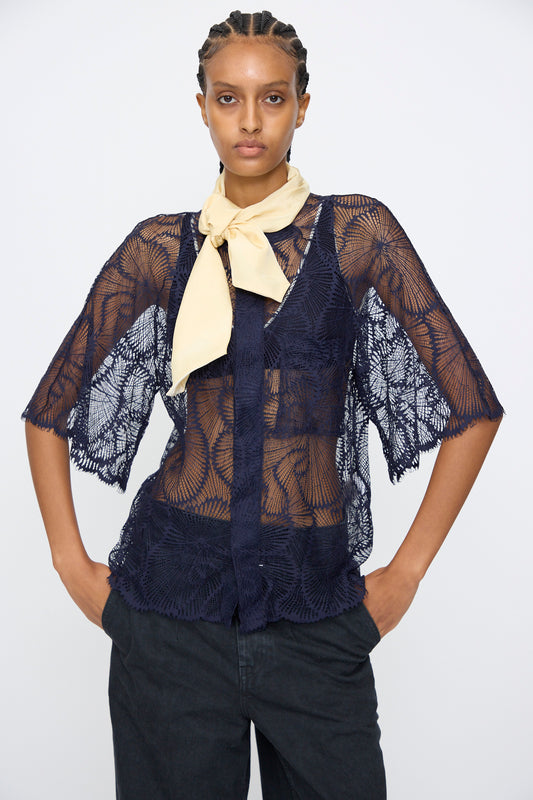 Model wears the TOGA ARCHIVES Lace Blouse in Navy with an oversized fit over a dark top, paired with black pants and a light beige neck scarf, standing hands on hips against a plain background.