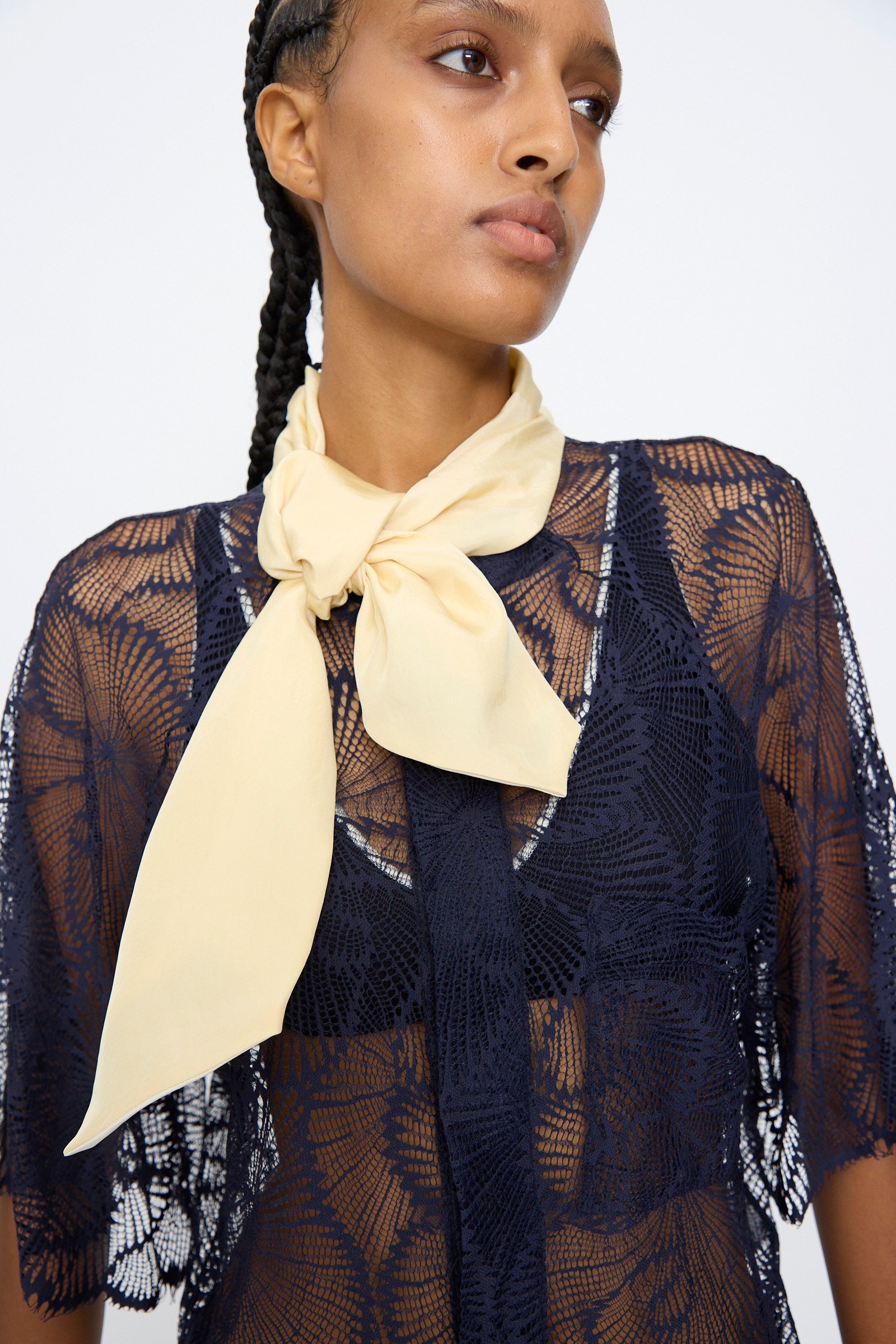 A person wears the TOGA ARCHIVES Lace Blouse in Navy with a cream scarf tied at the neckline, gazing slightly to the side against a plain background.