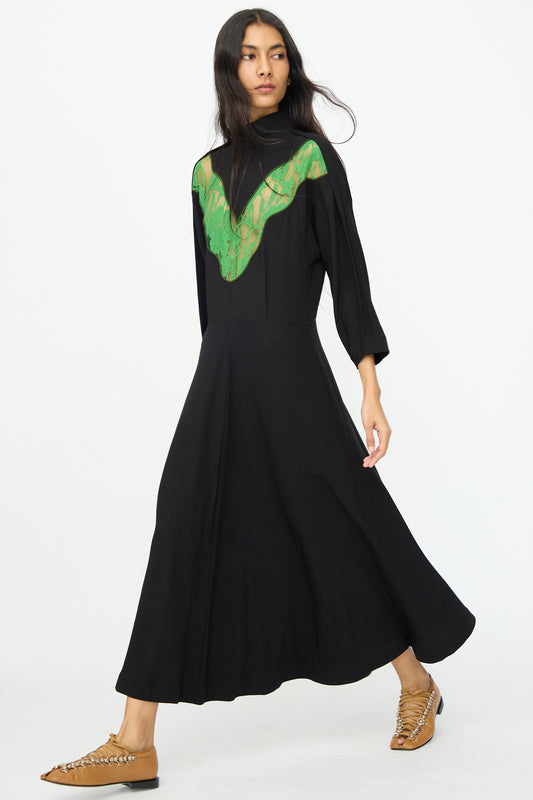 A woman wearing the TOGA ARCHIVES Lace Dress in Black with long sleeves, walking forward in tan flat shoes against a plain white background.