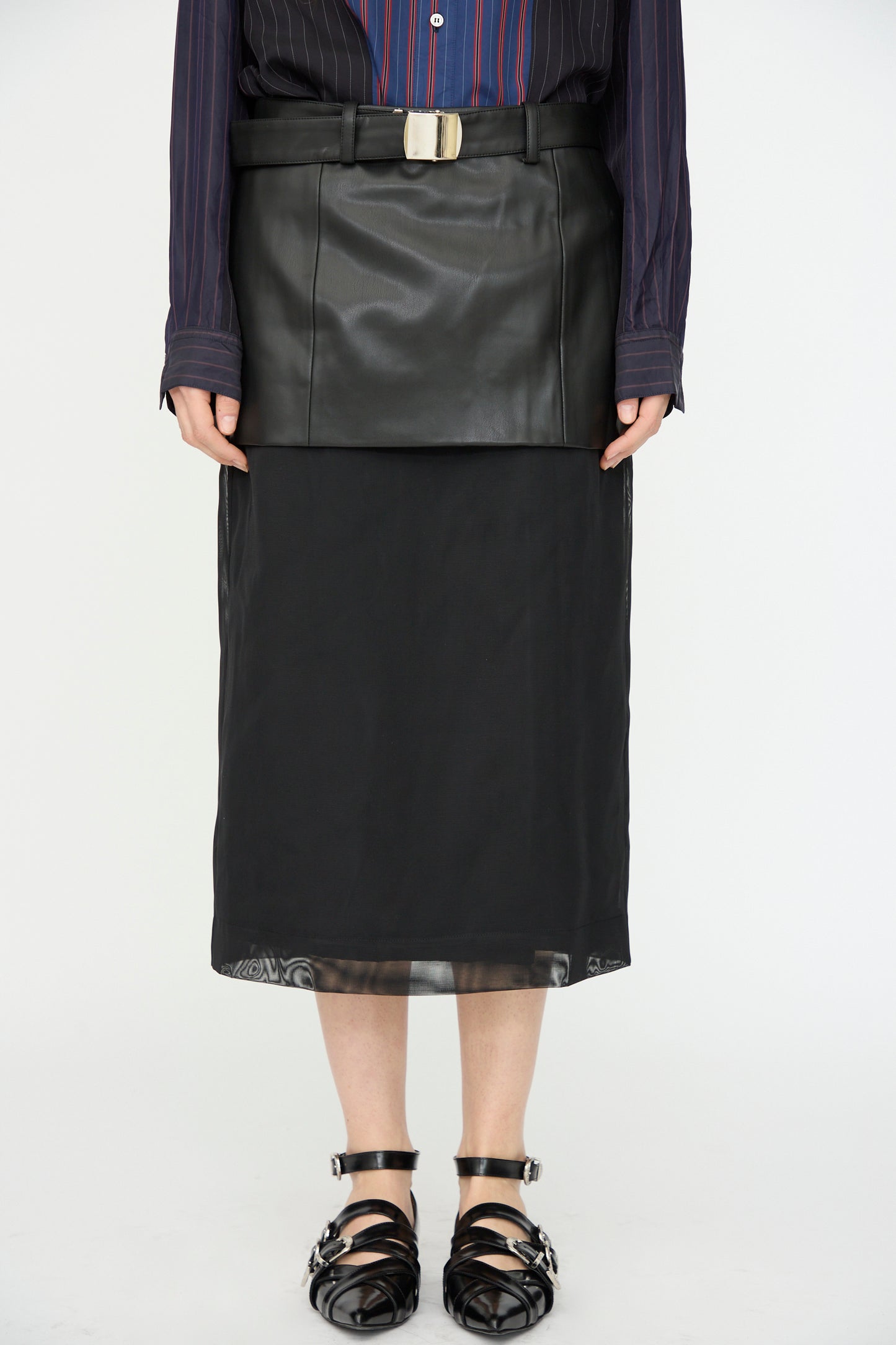 A person wearing the TOGA ARCHIVES Leather Mesh Skirt in Black, styled with a striped blouse and black strappy shoes.