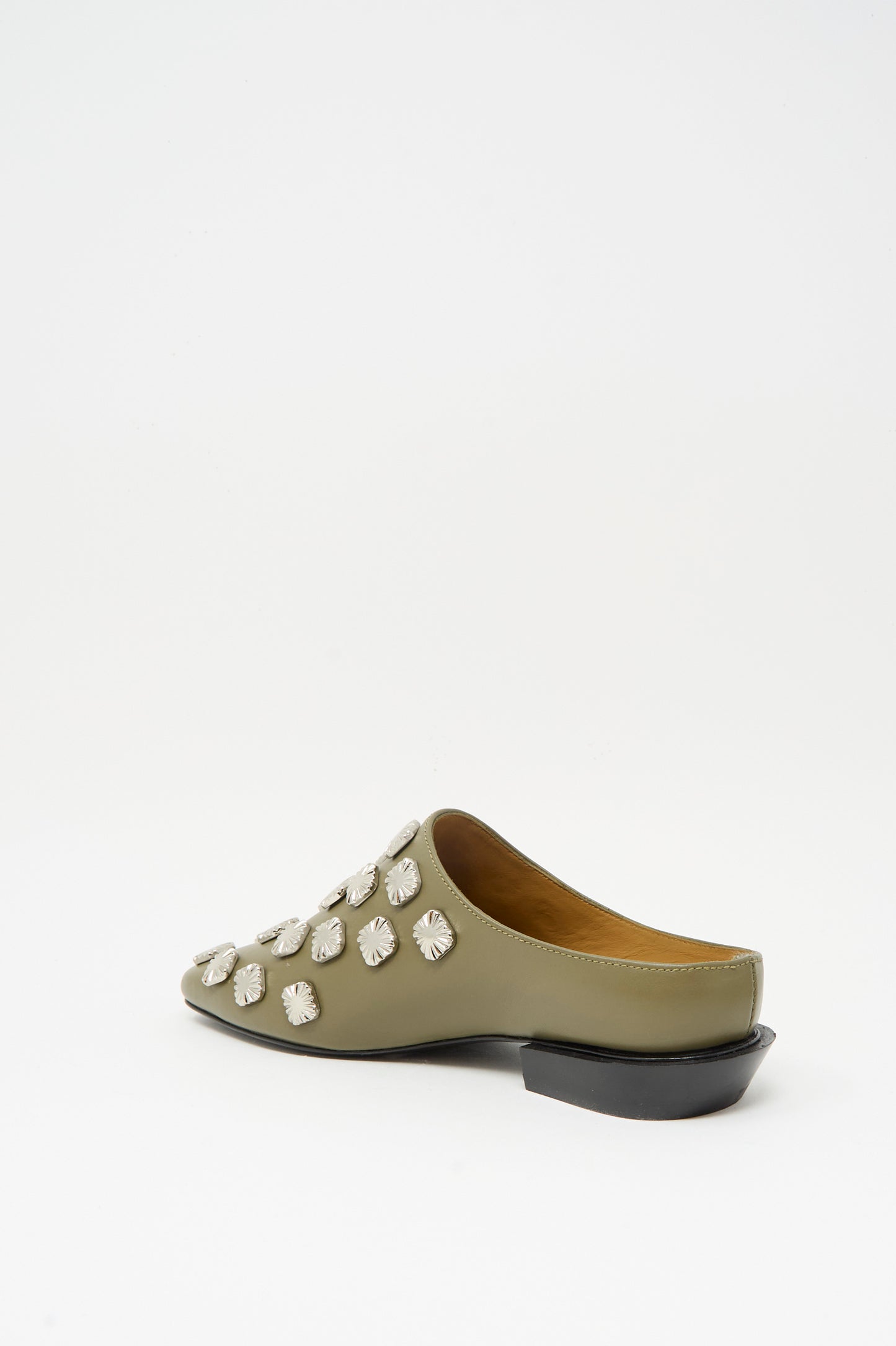 The Leather Mule in Khaki by TOGA ARCHIVES features decorative silver studs, a closed pointed toe, an open back, and a low black heel, displayed against a plain white background.