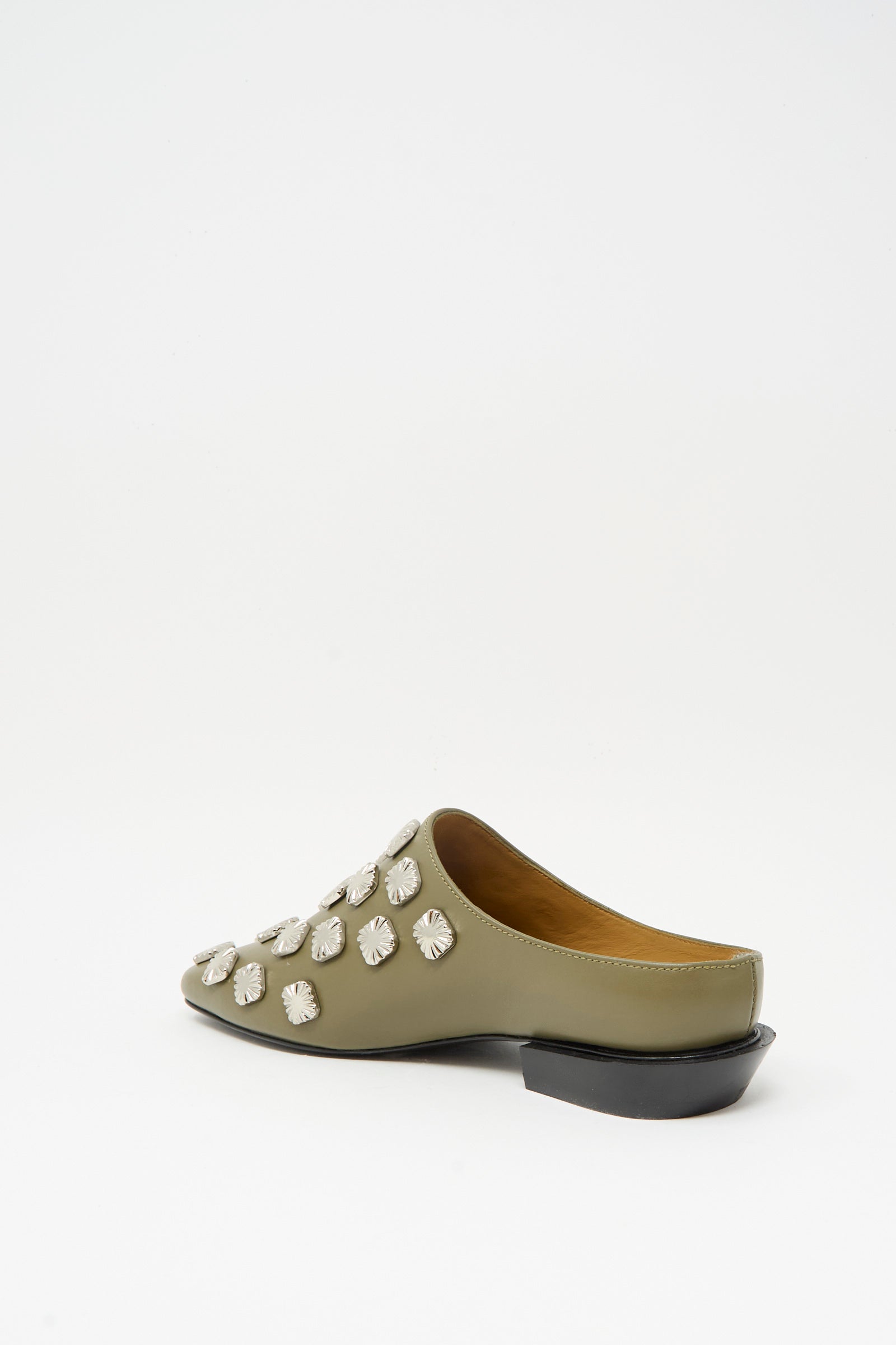 The Leather Mule in Khaki by TOGA ARCHIVES features decorative silver studs, a closed pointed toe, an open back, and a low black heel, displayed against a plain white background.
