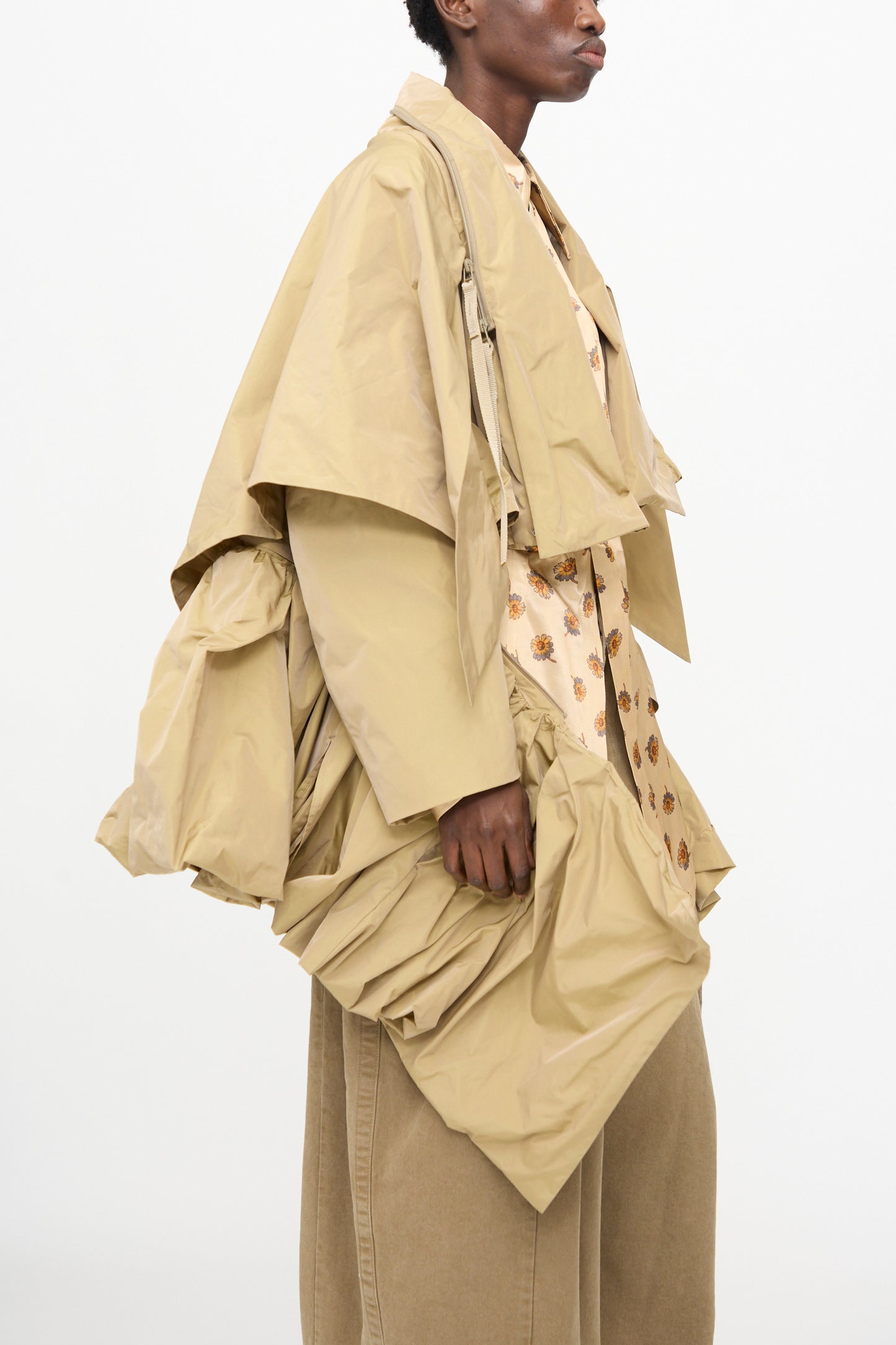 Someone wears TOGA ARCHIVES' Memory Taffeta Jacket in Beige, featuring sculptural, oversized ruched details, styled over a patterned shirt and wide-legged beige pants.