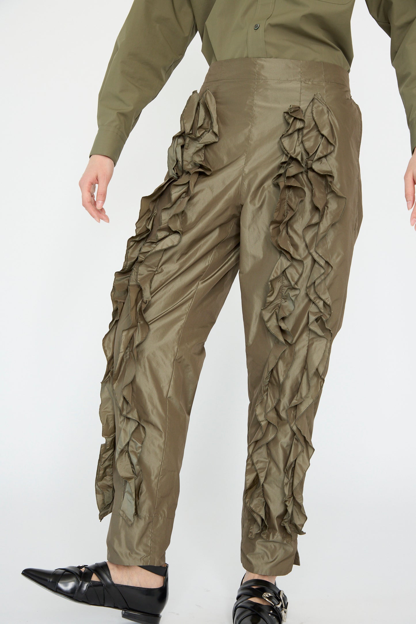 Wearing TOGA ARCHIVES' Memory Taffeta Pant in Khaki with a matching shirt and sleek black shoes against a white background, seen from below the shoulders.