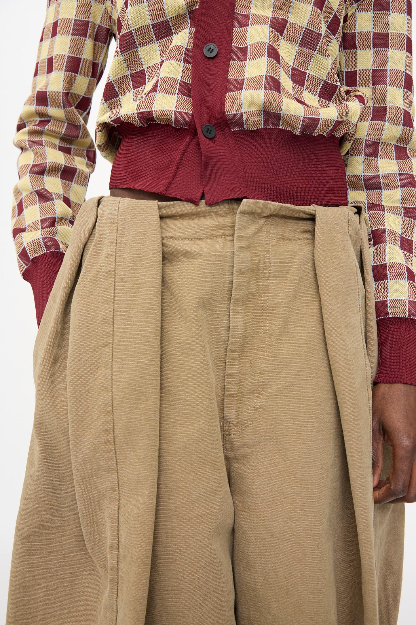 A person wearing a checkered maroon and beige sweater paired with TOGA ARCHIVES Oxford Wide Pants in Beige.