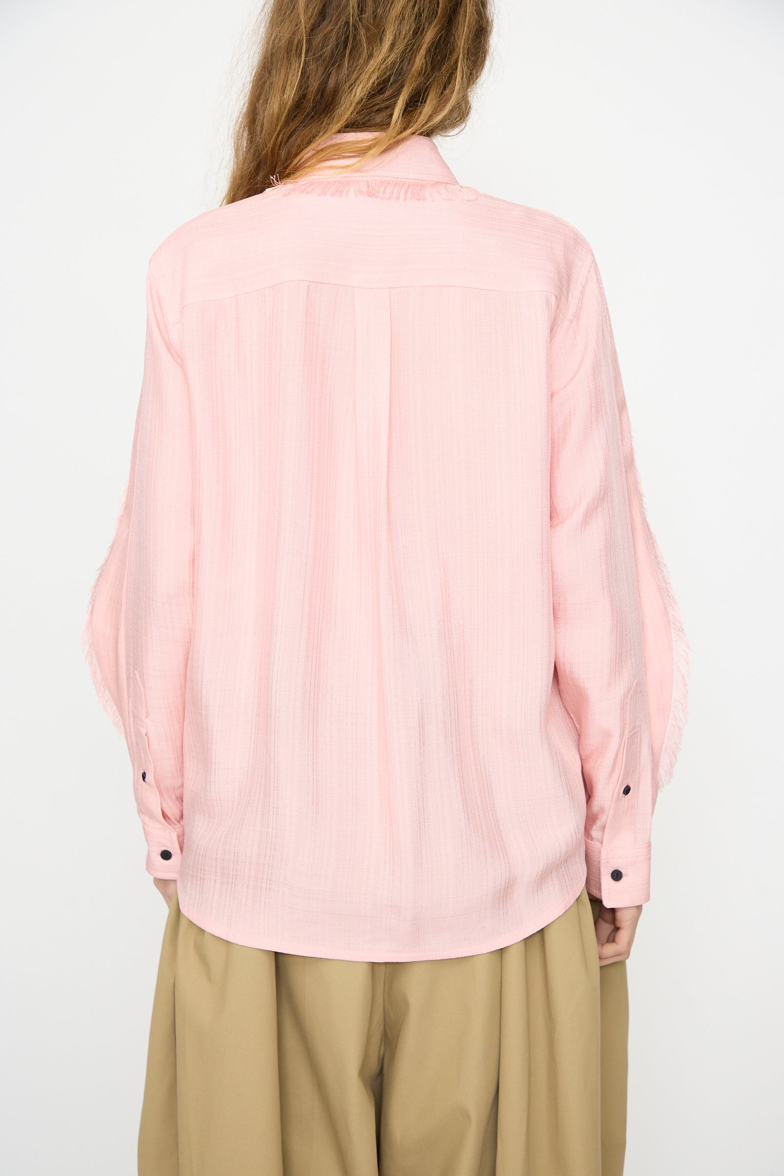 A person is shown from the back wearing the TOGA ARCHIVES Plain Weave Shirt in Pink with black cuff buttons and loose beige pants, set against a plain white background.