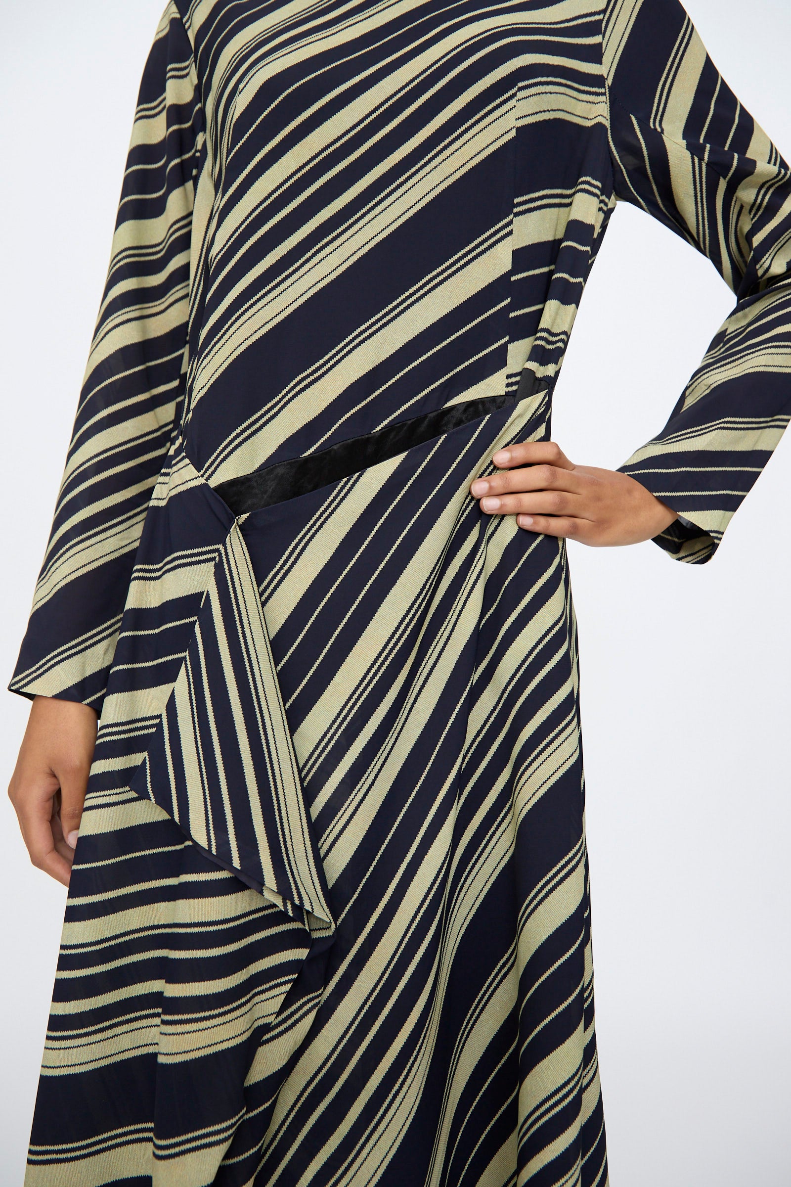 Person wears the TOGA ARCHIVES Rayon Print Dress in Navy, a long-sleeve maxi with black and beige diagonal stripes and draped waist detail; crafted from printed rayon and made in Japan.