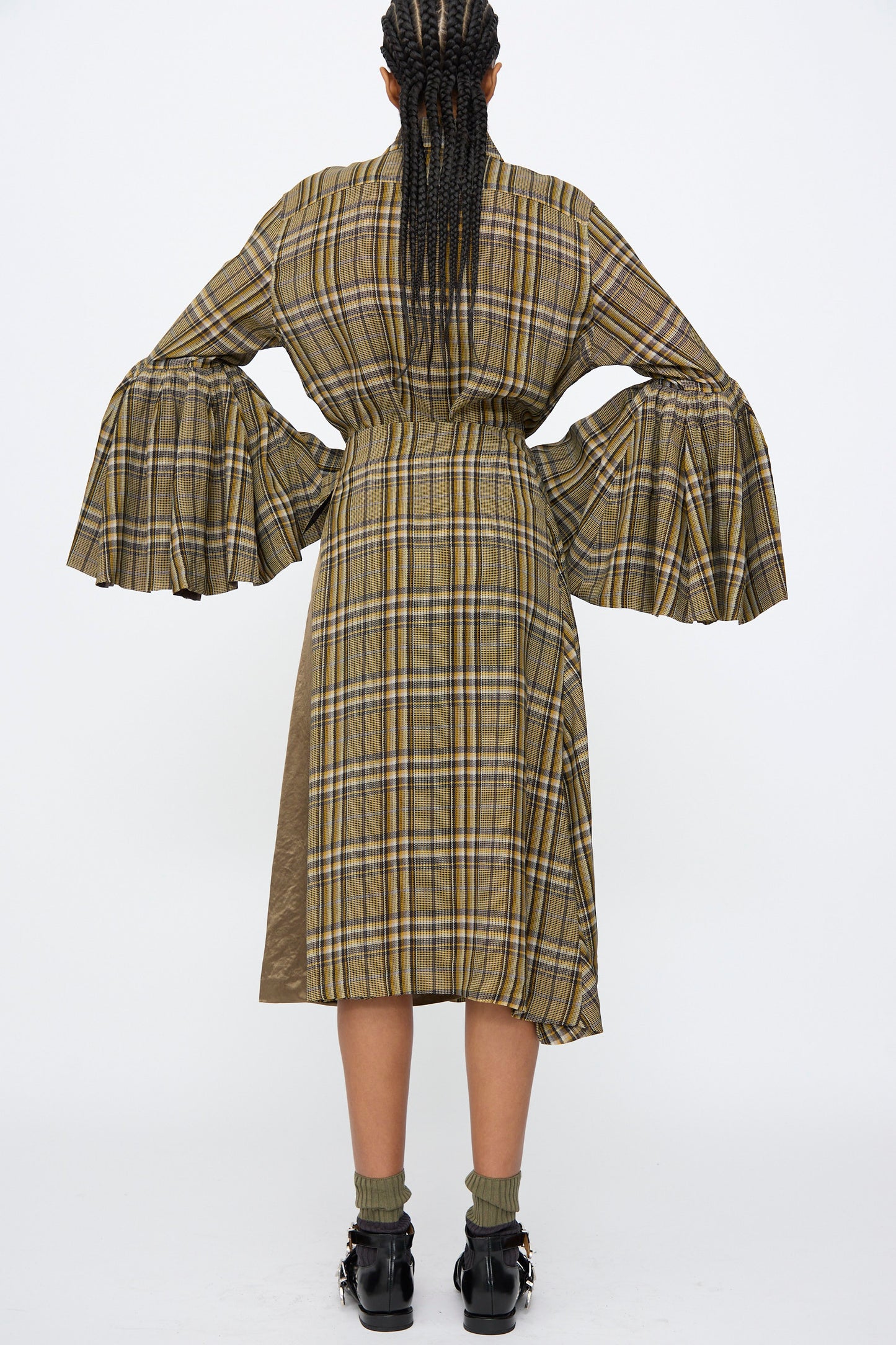 A person with braided hair wears the TOGA ARCHIVES Rayon Print Skirt in Brown, paired with wide bell sleeves, green socks, and black shoes.