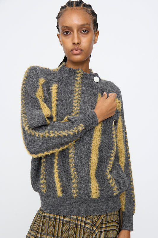 A person wears the TOGA ARCHIVES Stripe Knit Pullover in Gray, featuring yellow textured stripes, paired with a plaid skirt, standing against a plain light background and looking directly at the camera.