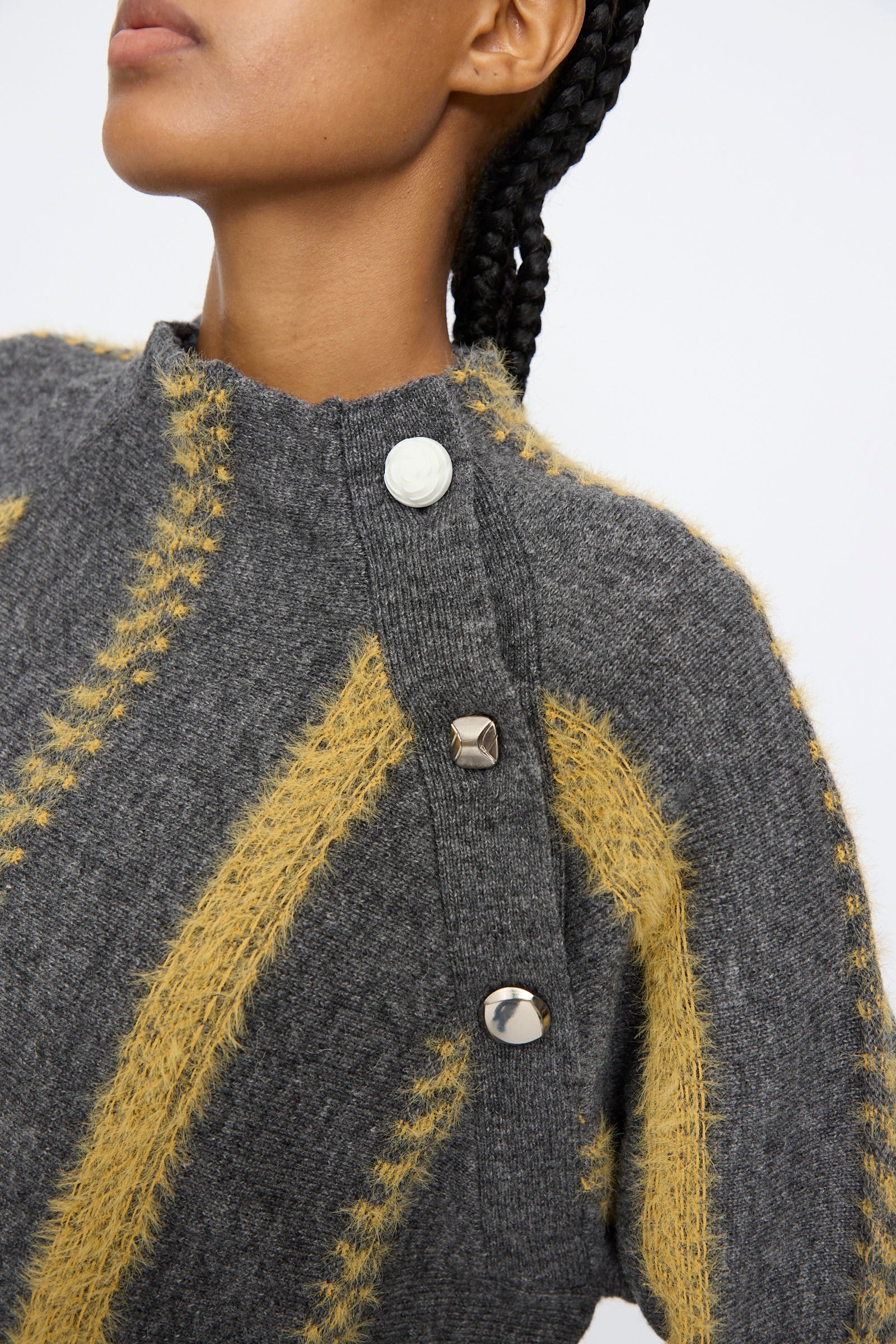 A person is shown wearing the TOGA ARCHIVES Stripe Knit Pullover in Gray, a wool blend sweater with yellow stripes and large shoulder buttons; only the lower half of their face and upper torso are visible.