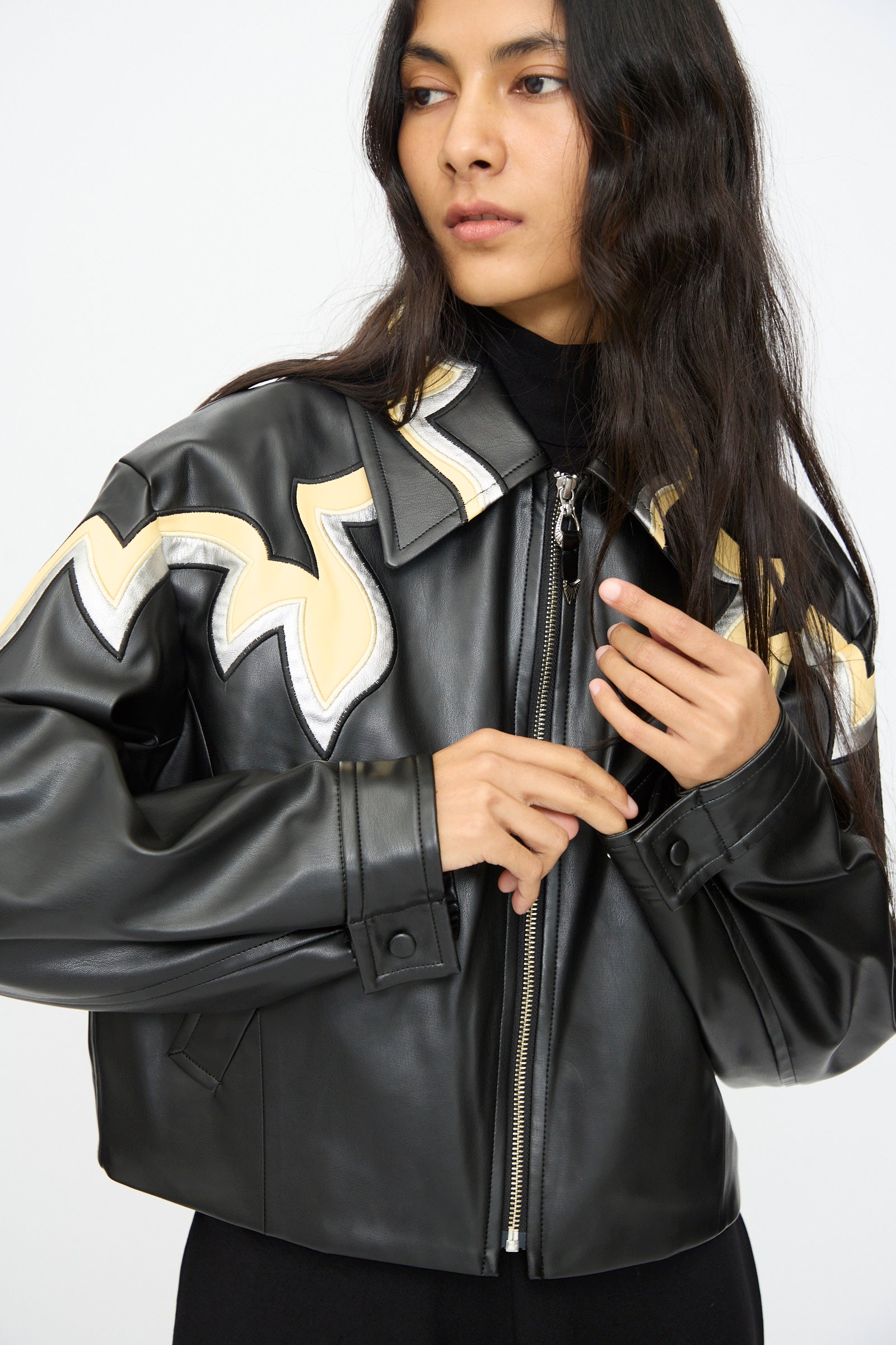 A person wears the TOGA ARCHIVES Synthetic Leather Jacket in Black, featuring cream and white western-inspired zigzag patterns, against a plain light background.