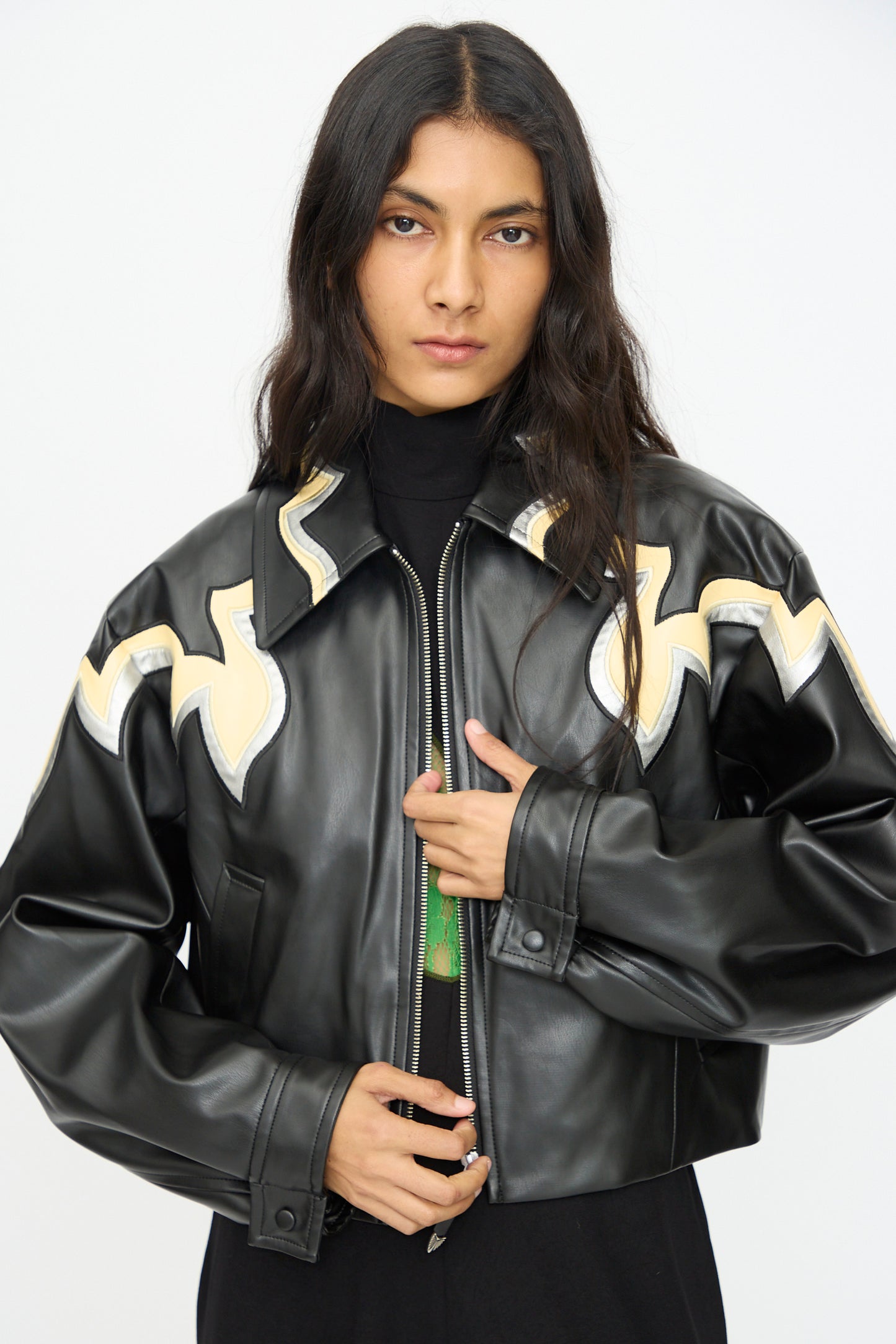 Model wears the TOGA ARCHIVES Synthetic Leather Jacket in Black, featuring beige abstract designs, standing against a plain light background and looking at the camera with a neutral expression.