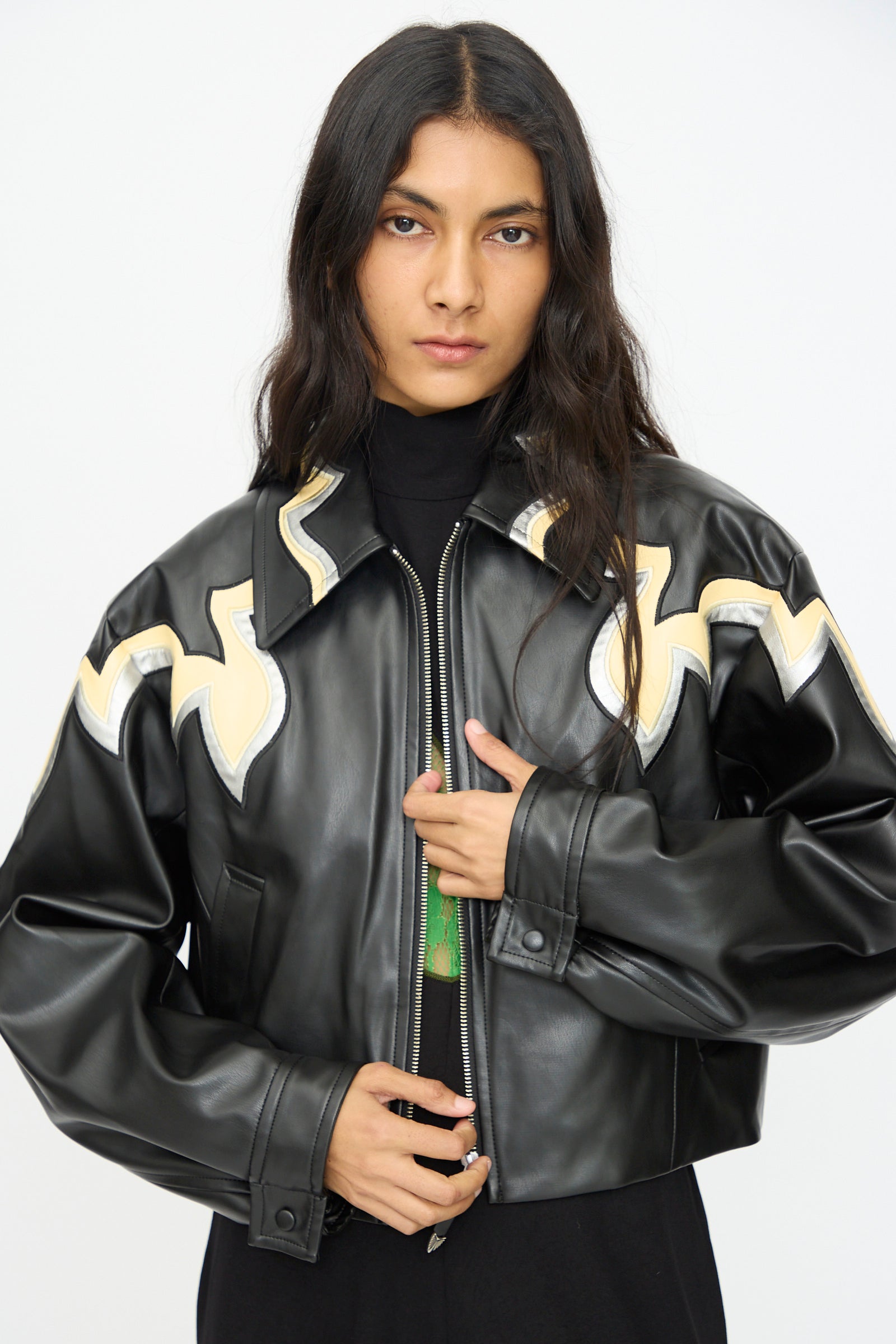 Model wears the TOGA ARCHIVES Synthetic Leather Jacket in Black, featuring beige abstract designs, standing against a plain light background and looking at the camera with a neutral expression.