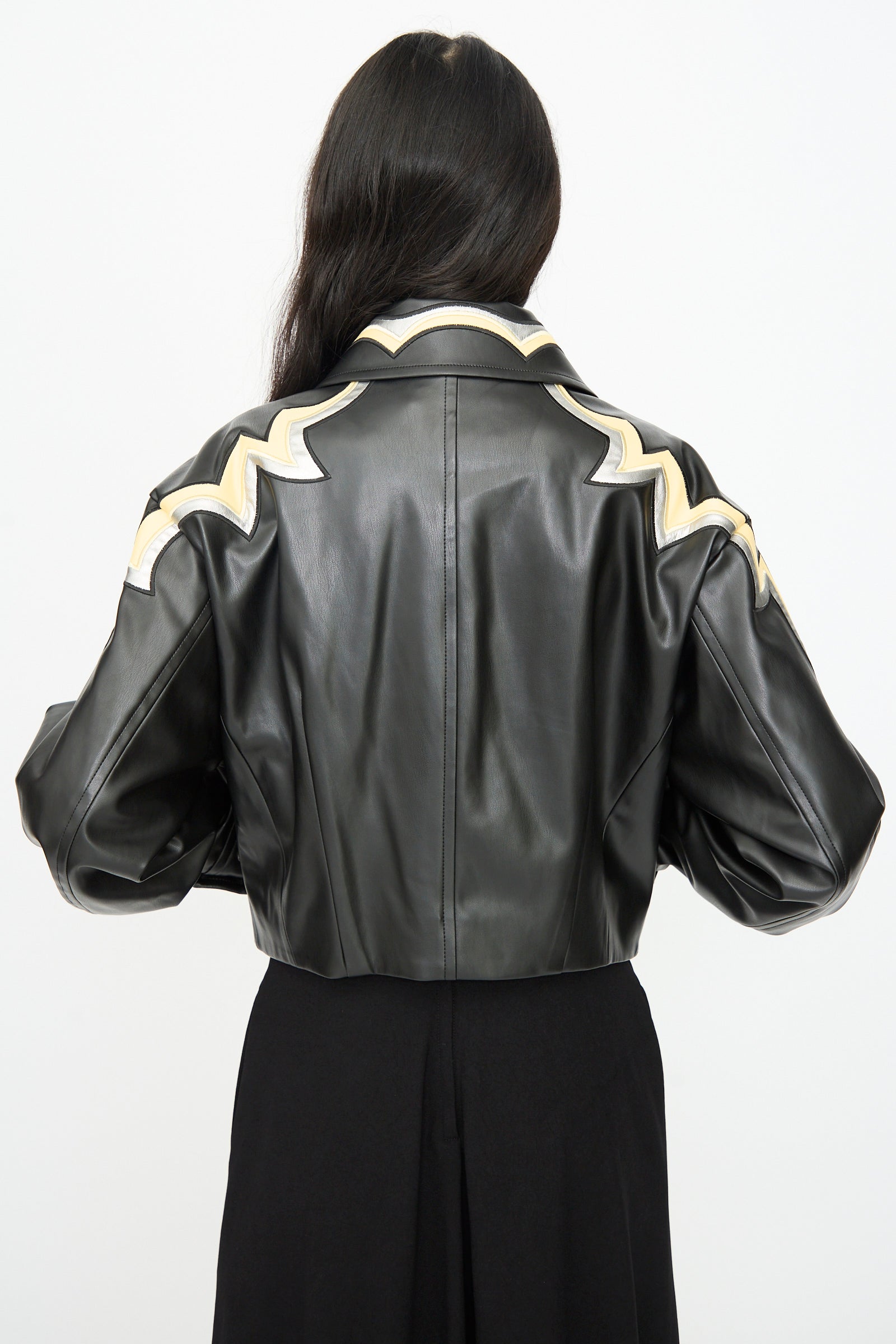 A person with long dark hair, seen from behind, wears the TOGA ARCHIVES Synthetic Leather Jacket in Black with beige and white zigzag western detail on the shoulders, photographed against a plain background.