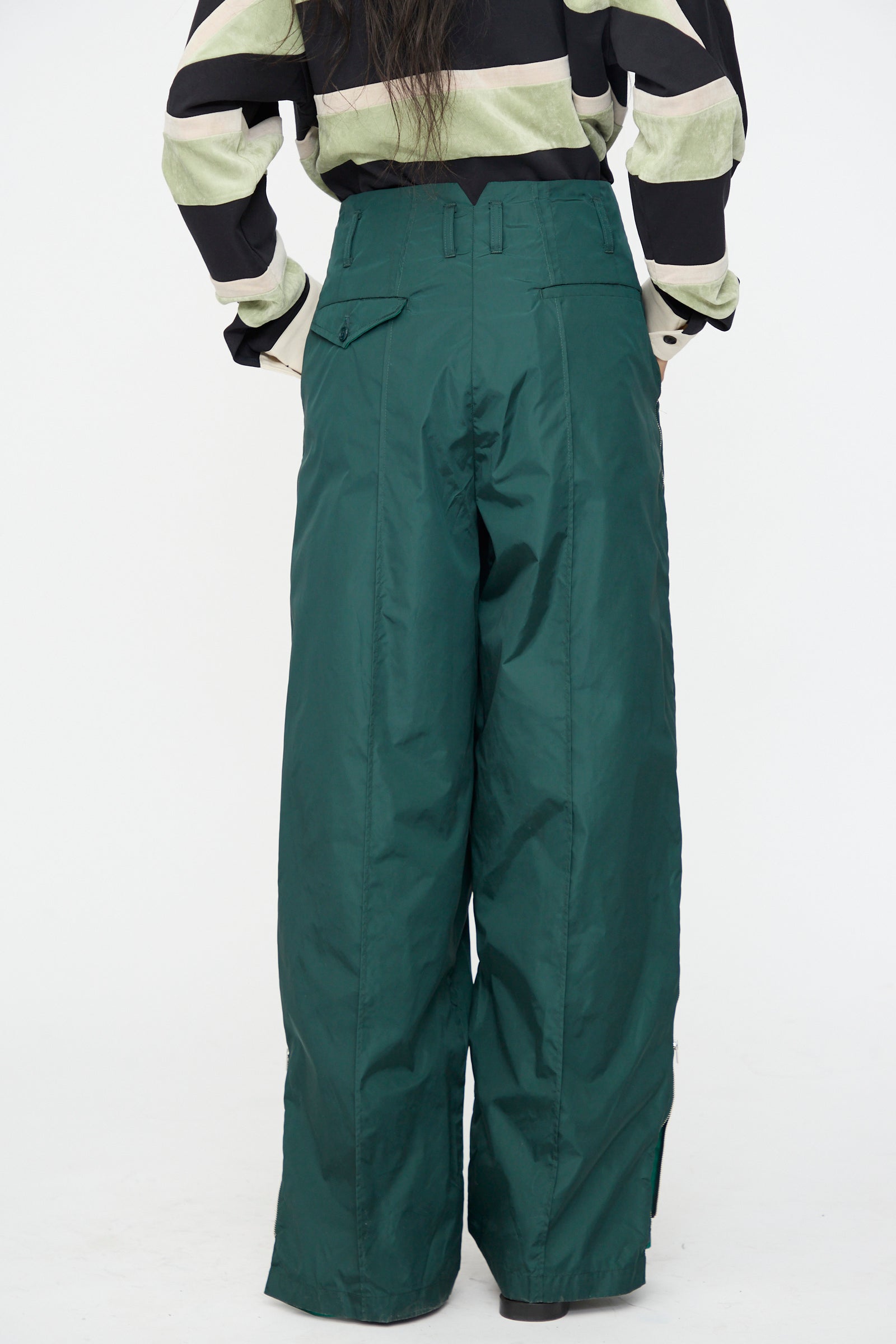 Model wearing the TOGA ARCHIVES Taffeta Zip Pant in Green with a black-and-white striped long-sleeve top, seen from the back against a plain white background.