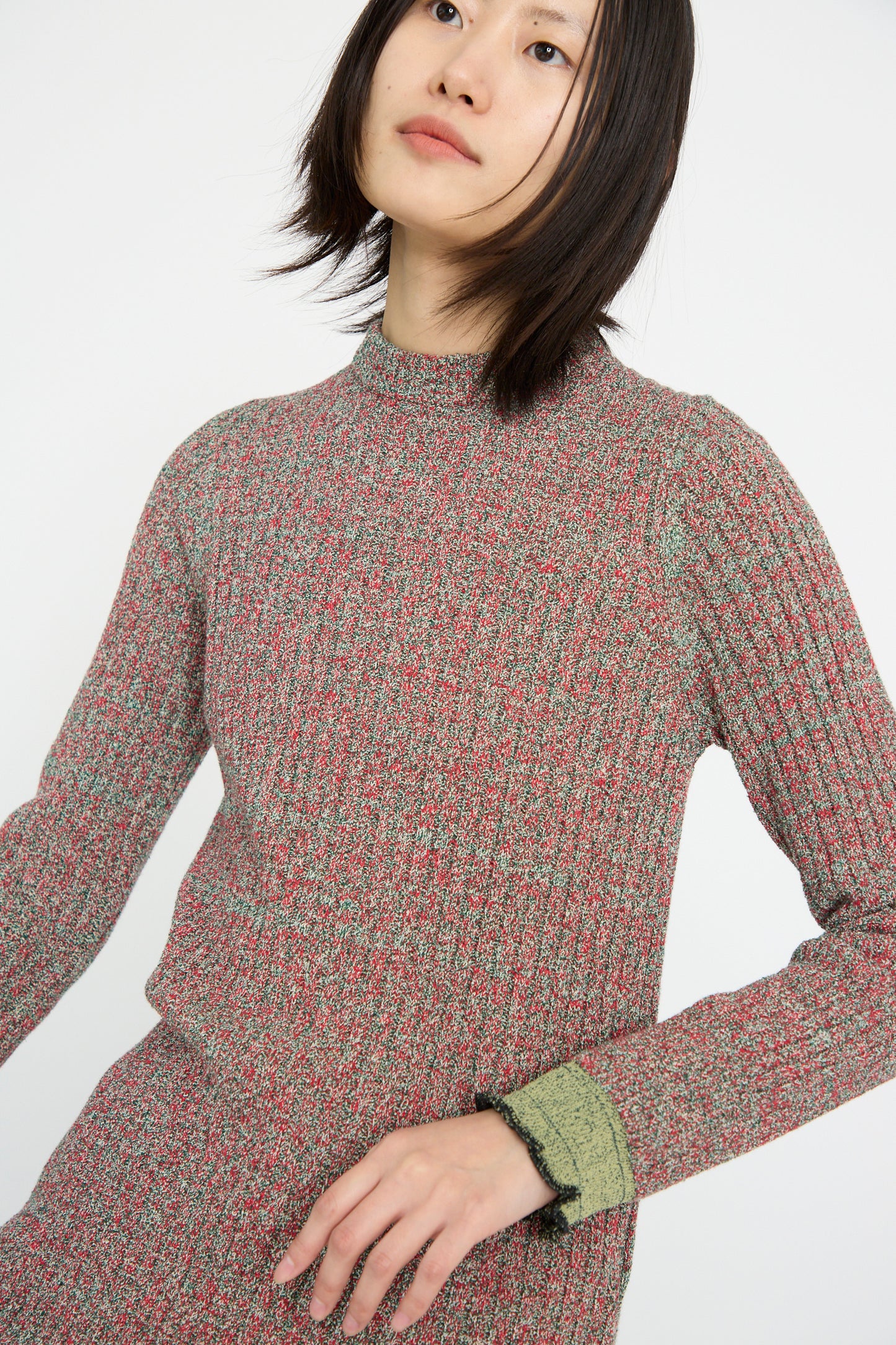 A person wearing a Tweed Knit Back Zip Pullover in Green by TOGA ARCHIVES, gazing upward with a neutral expression against a plain background.