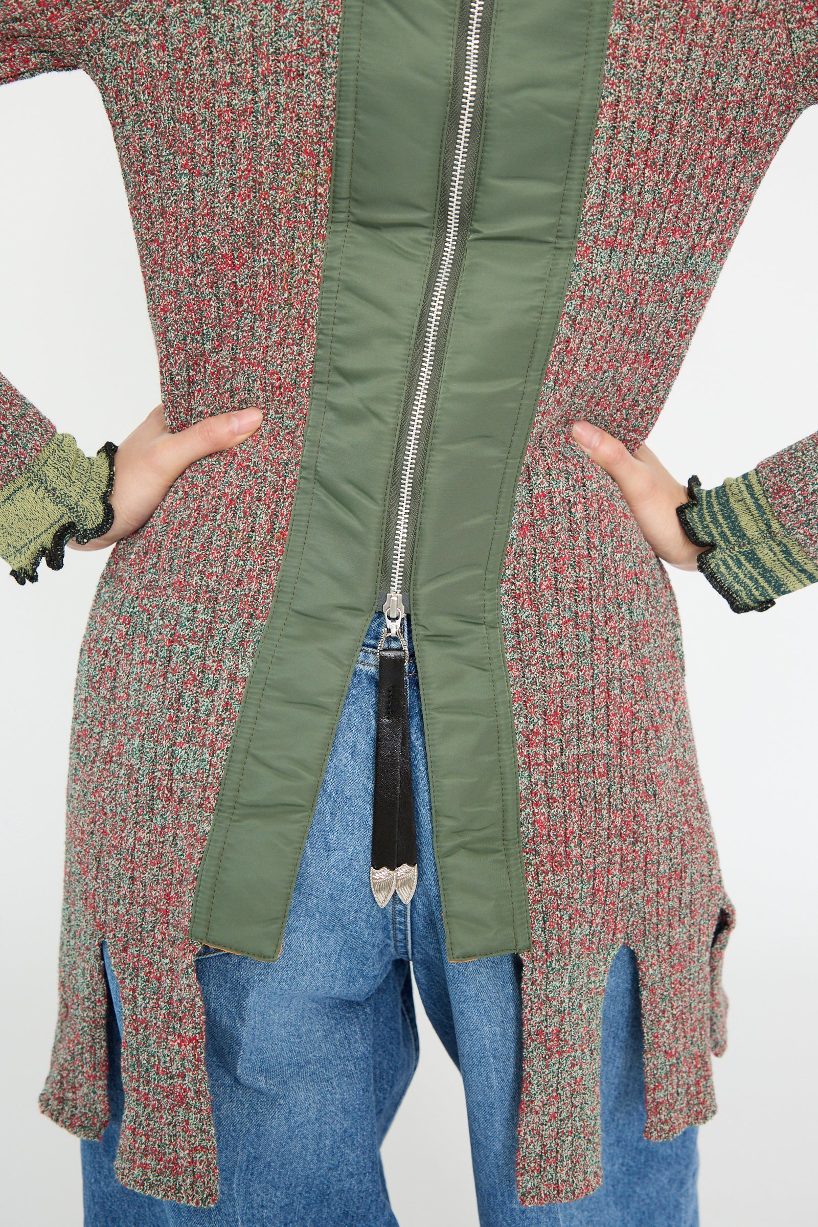 Back view of a person wearing the Tweed Knit Back Zip Pullover in Green by TOGA ARCHIVES, paired with blue fringe hem jeans. Hands rest on hips against a plain background. 