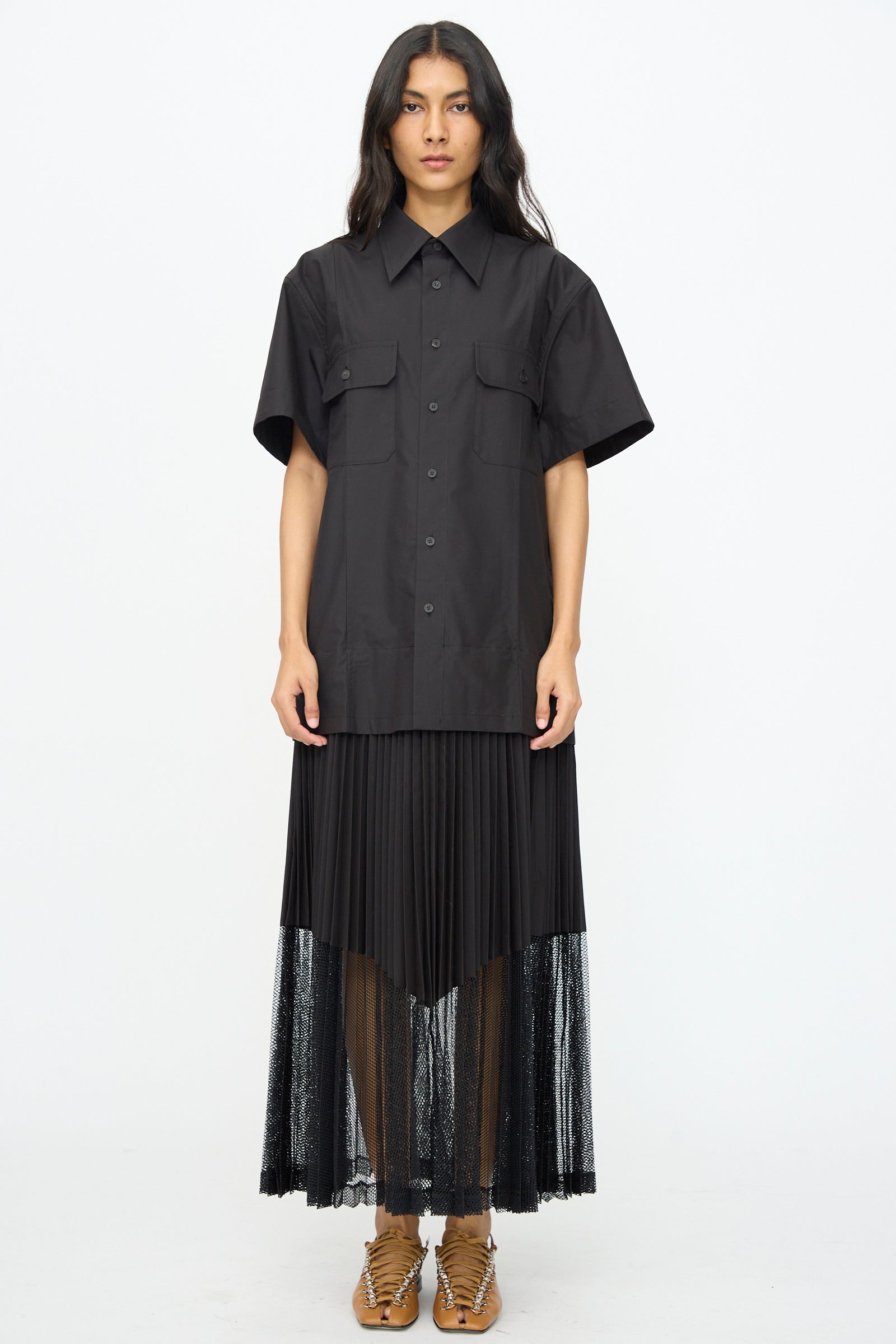A person faces forward wearing the TOGA ARCHIVES Typewriter Mesh Dress in Black, featuring a shiny cotton blend and mesh hem, styled with tan lace-up shoes.
