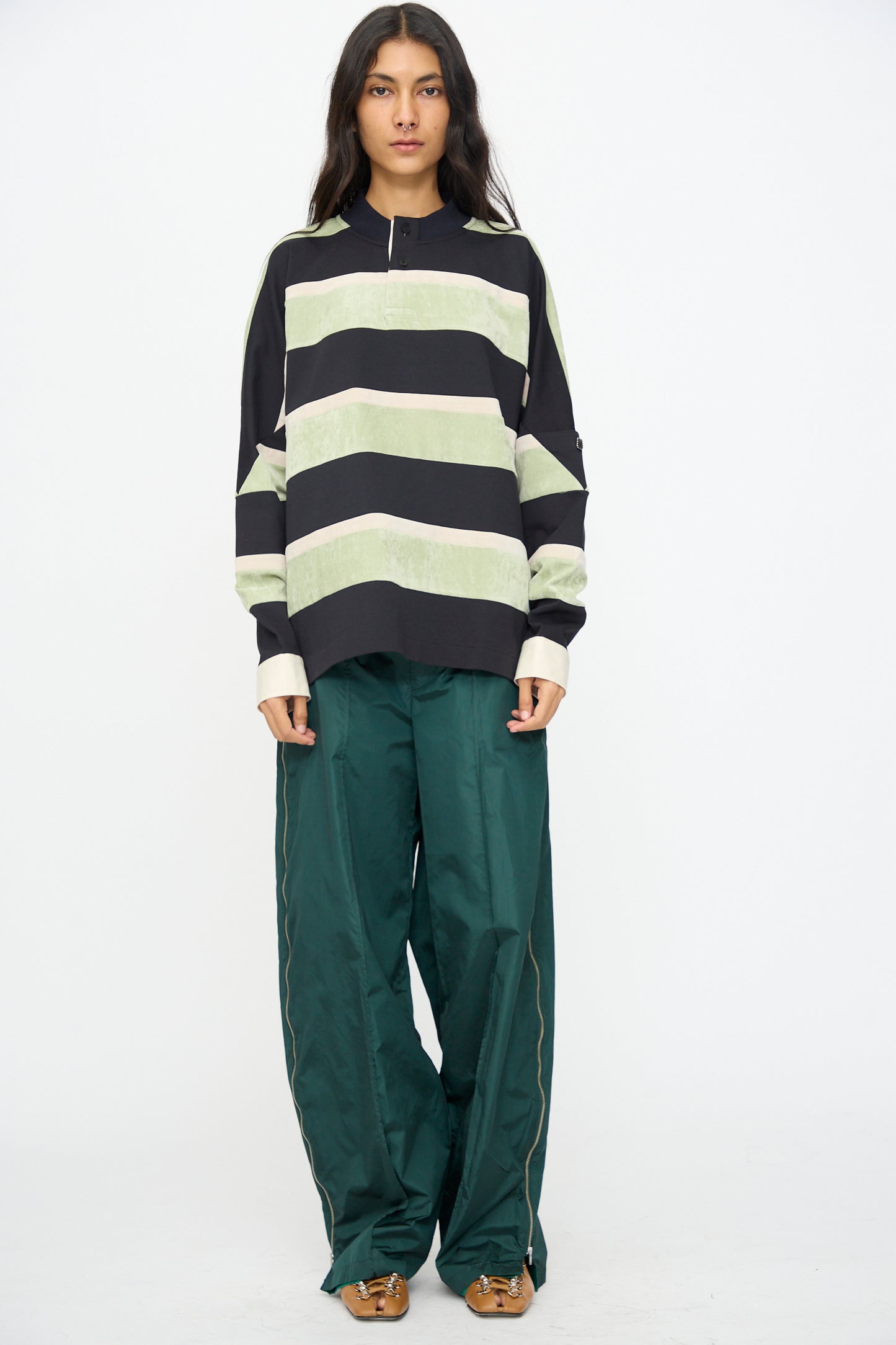 A person stands facing forward against a plain white background, wearing the TOGA ARCHIVES Velvet Border Jersey Long Sleeve in Light Green with loose green pants and brown shoes.