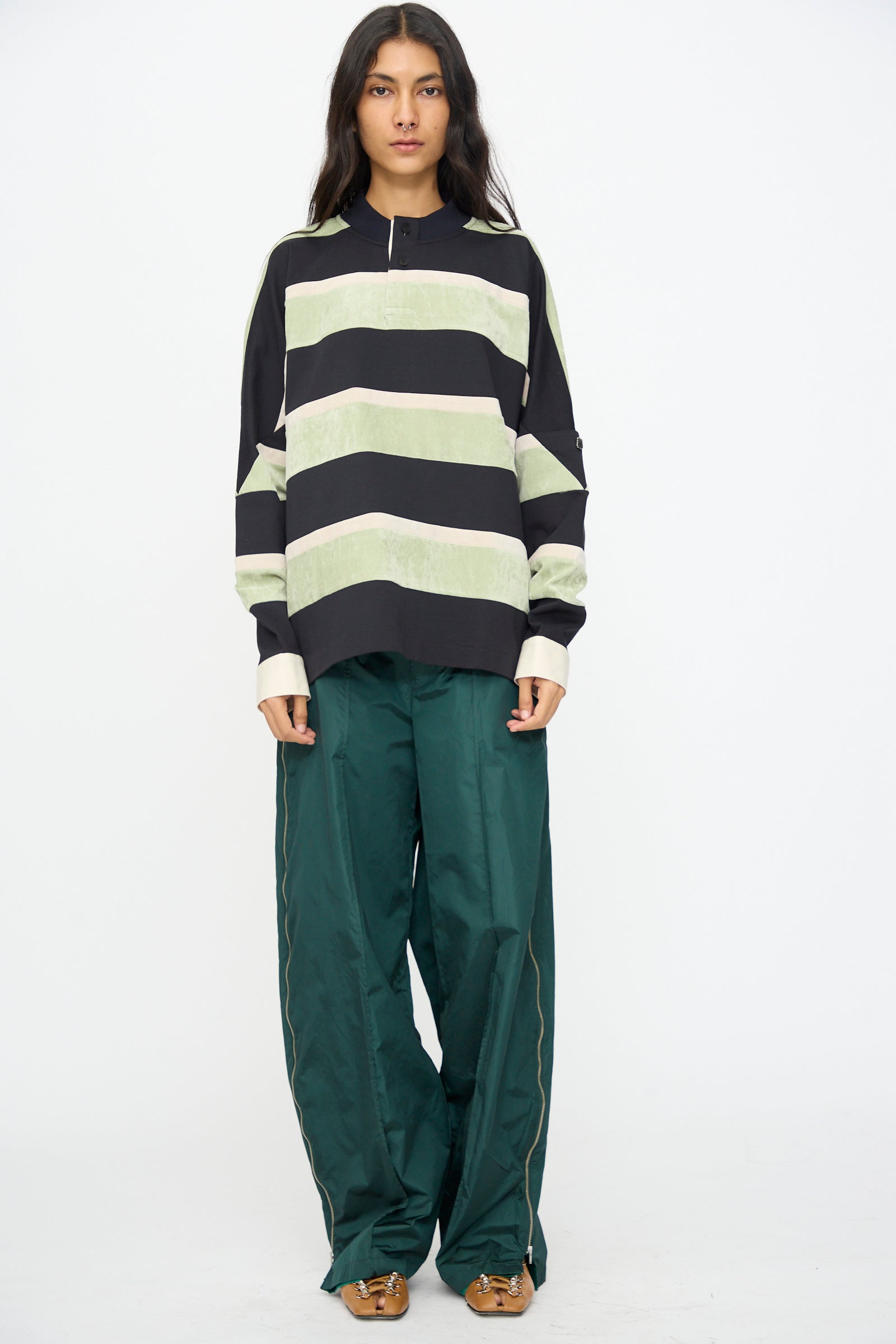 A person stands facing forward against a plain white background, wearing the TOGA ARCHIVES Velvet Border Jersey Long Sleeve in Light Green with loose green pants and brown shoes.