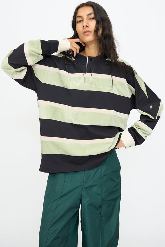 A person wearing the TOGA ARCHIVES Velvet Border Jersey Long Sleeve in light green with green pants, standing against a plain white background.