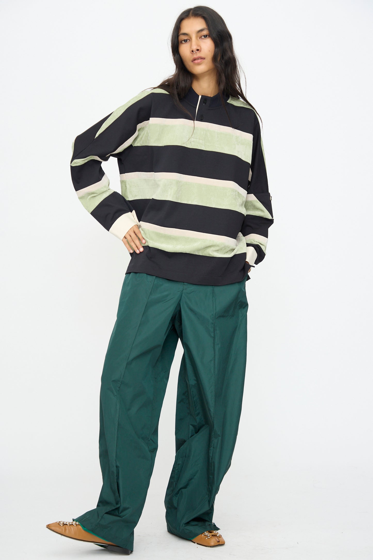 A person is standing against a white background, wearing the TOGA ARCHIVES Velvet Border Jersey Long Sleeve in light green, paired with wide green pants and brown shoes.