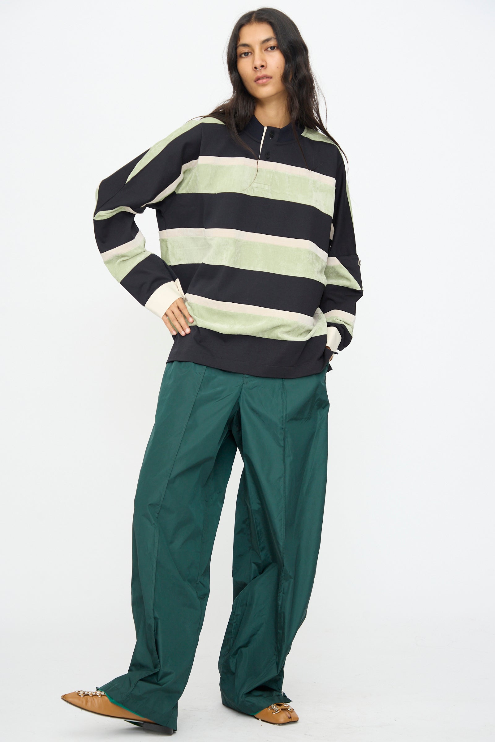 A person is standing against a white background, wearing the TOGA ARCHIVES Velvet Border Jersey Long Sleeve in light green, paired with wide green pants and brown shoes.
