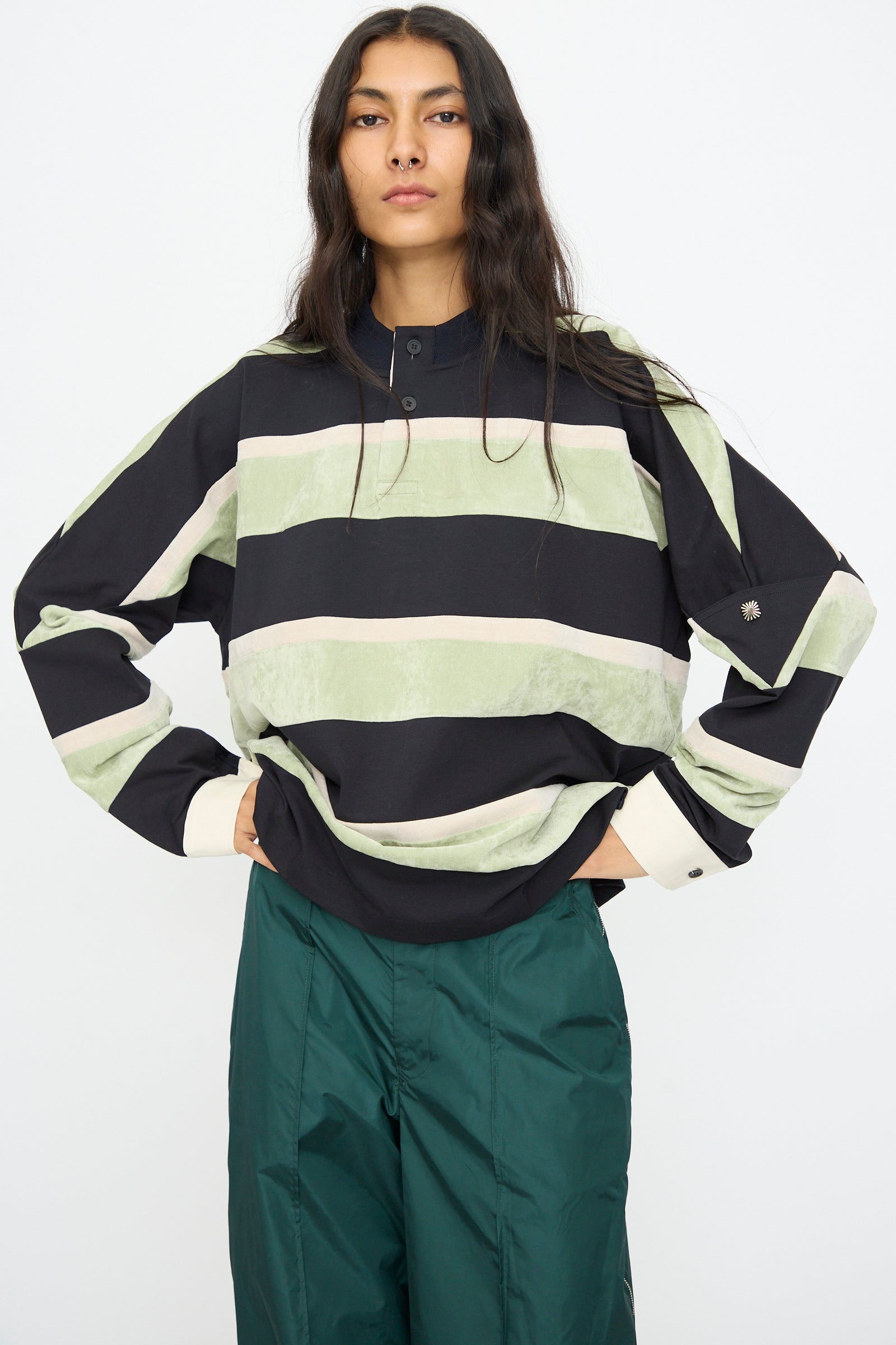 A woman stands with hands on hips, wearing the TOGA ARCHIVES Velvet Border Jersey Long Sleeve in Light Green and teal pants against a plain white background.