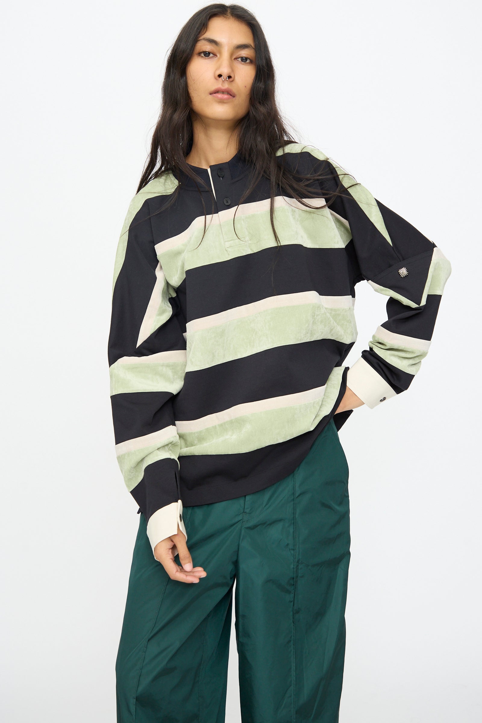 A person wears the TOGA ARCHIVES Velvet Border Jersey Long Sleeve in Light Green with dark green pants, standing against a plain white background.